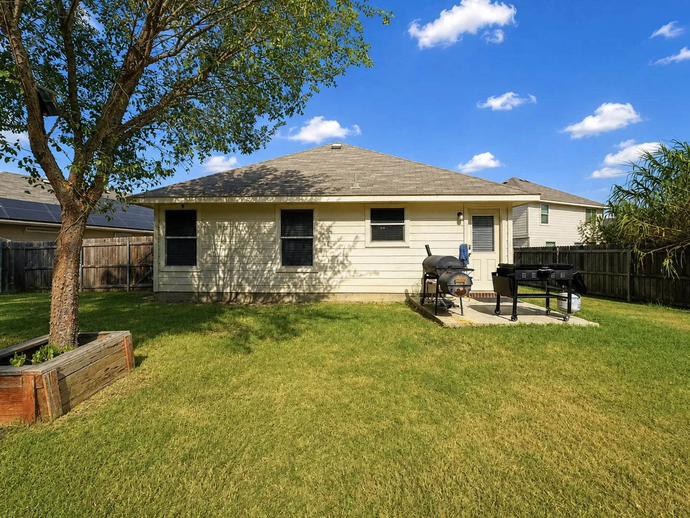 Expansive backyard featuring a manicured lawn, established tree, wood raised planter, and a concrete patio pad