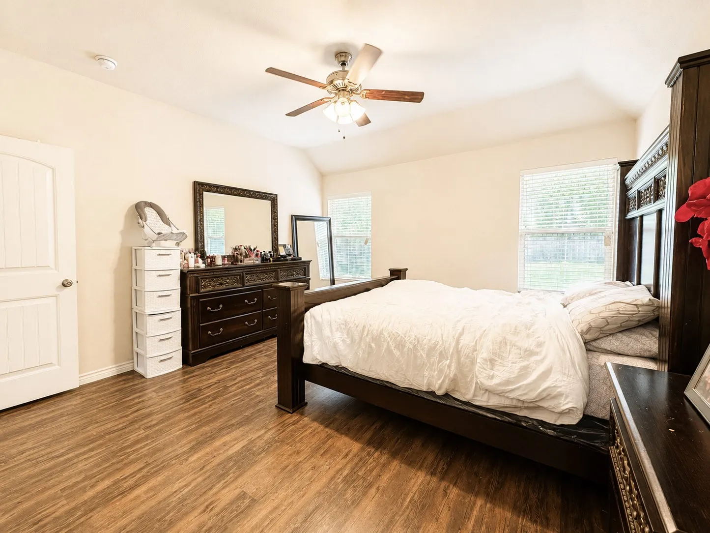 Vaulted ceiling with a ceiling fan, wood-finish flooring, two windows with blinds, and a paneled door