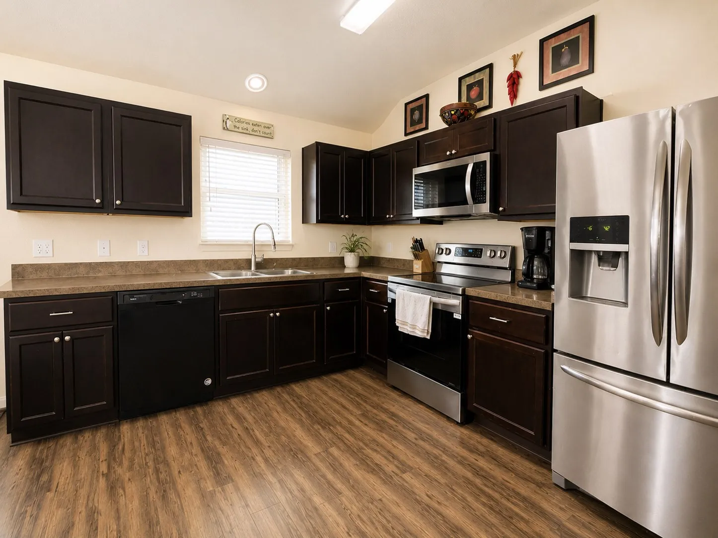 Kitchen featuring dark wood-finish cabinetry, stainless steel appliances, wood-finish flooring, and a double basin sink