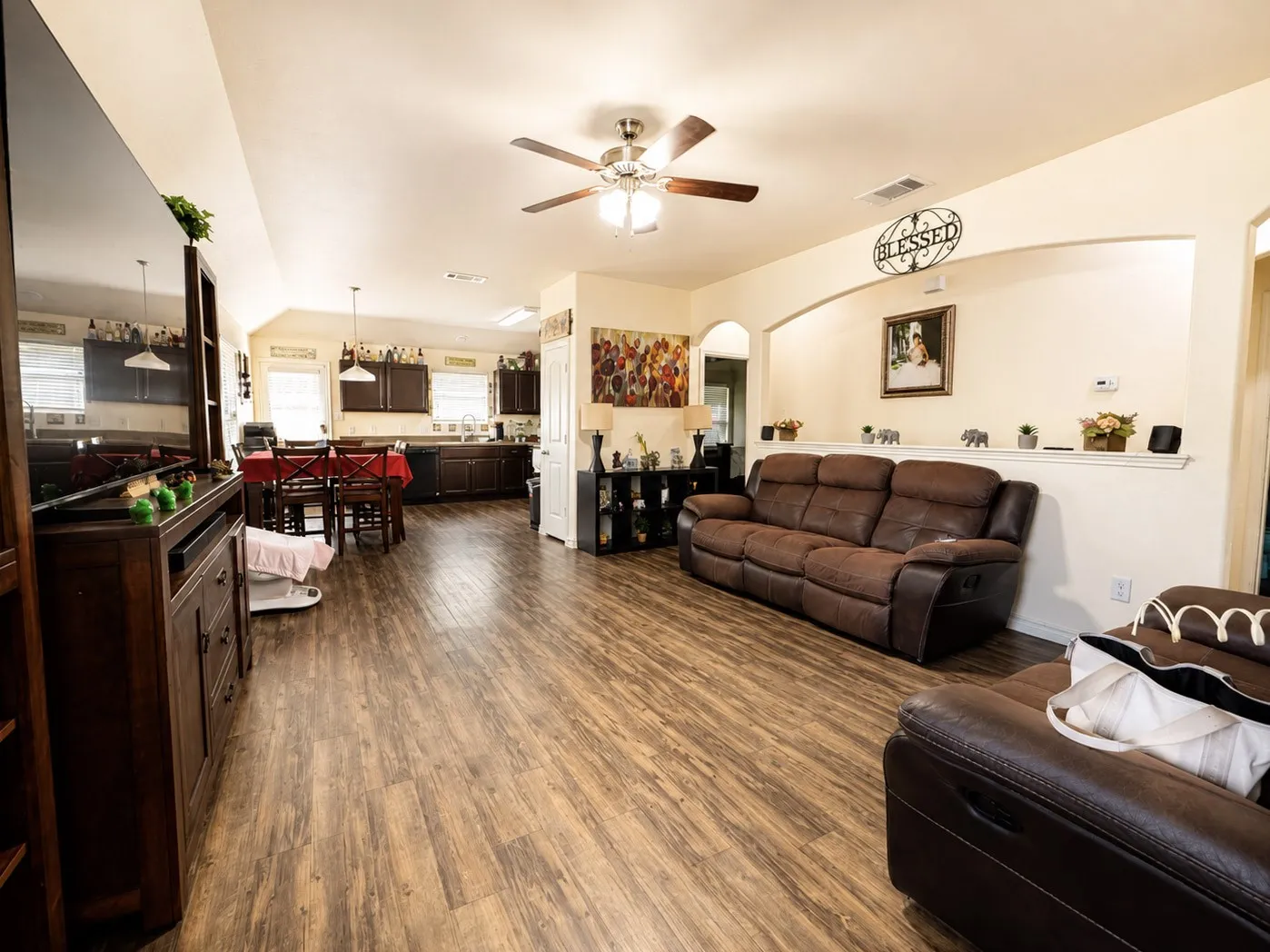 Open-concept living area with wood-finish flooring, a ceiling fan, and an arched wall feature