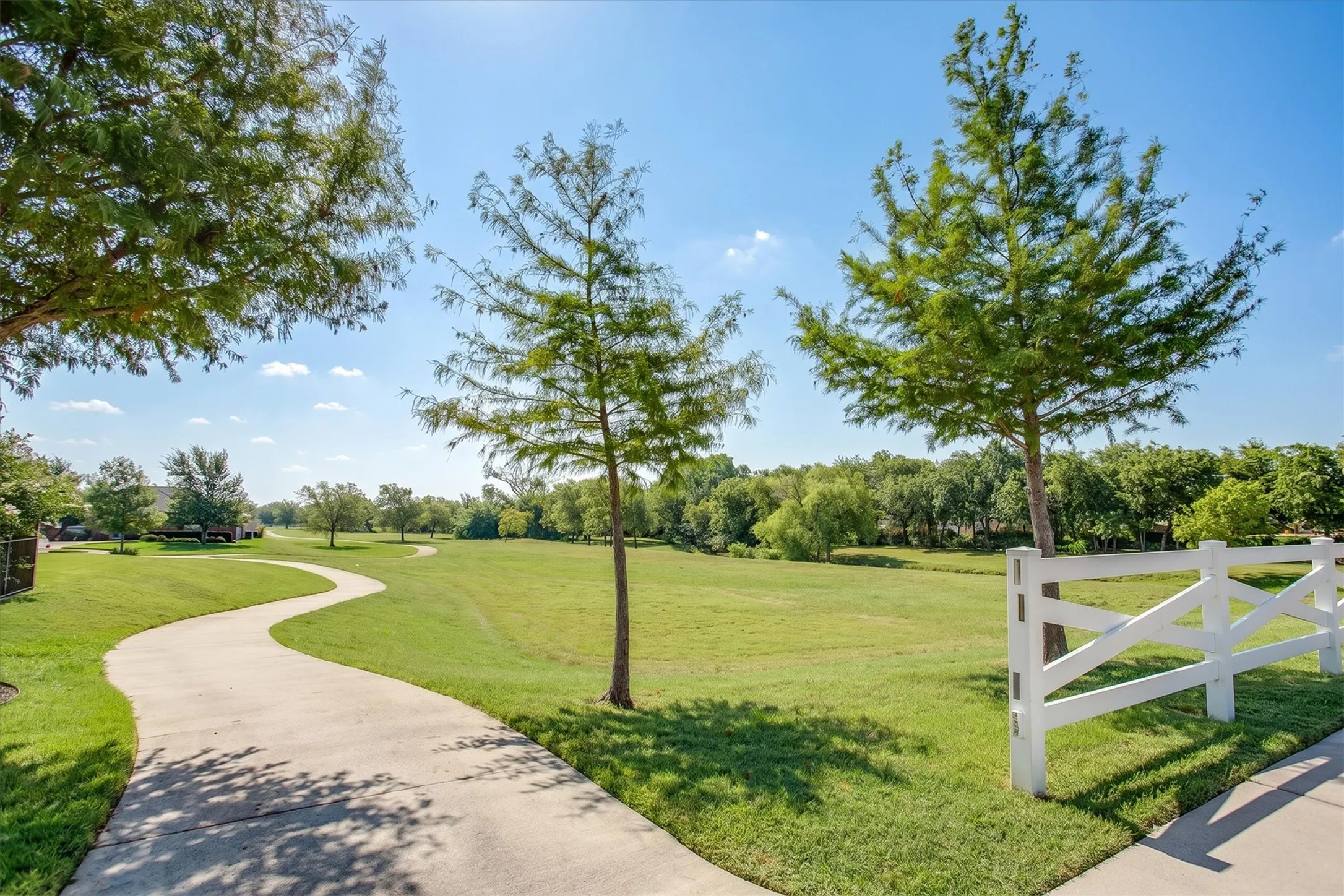 Scenic community walking path lined with trees and a classic white fence
