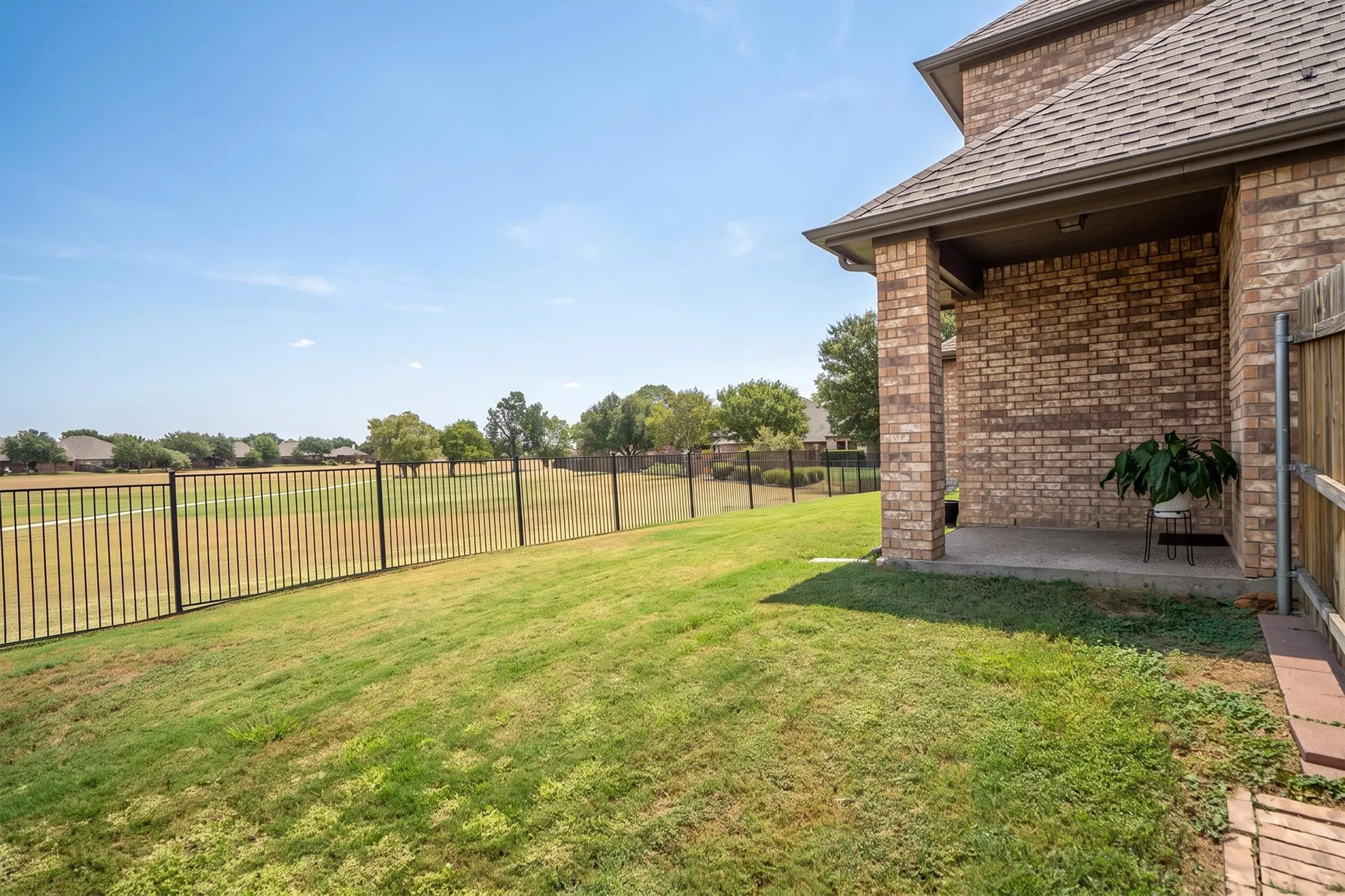 Covered back patio overlooking a fully fenced backyard with open space beyond