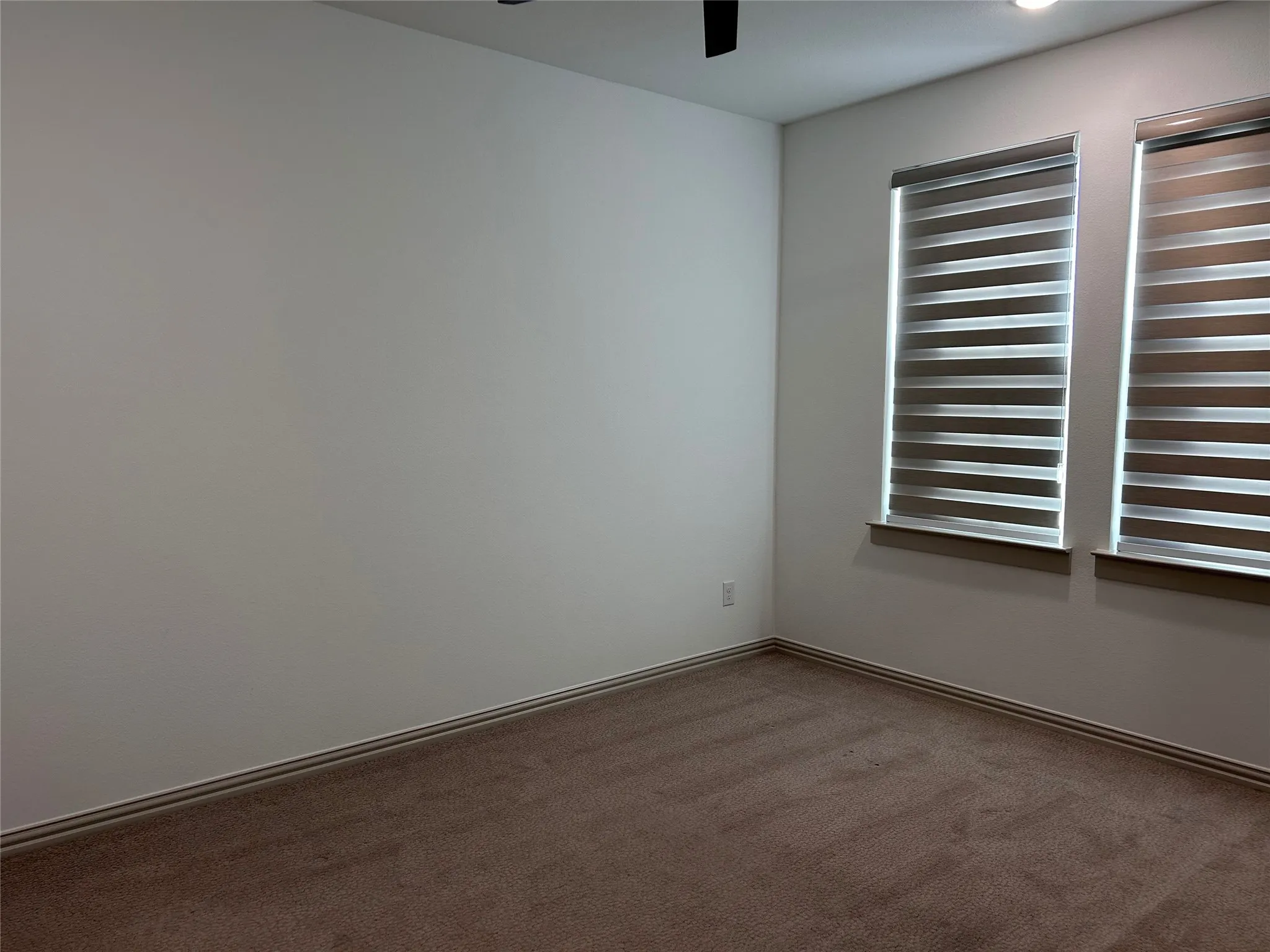 White walls with brown carpet flooring, featuring two windows with horizontal blinds and recessed lighting