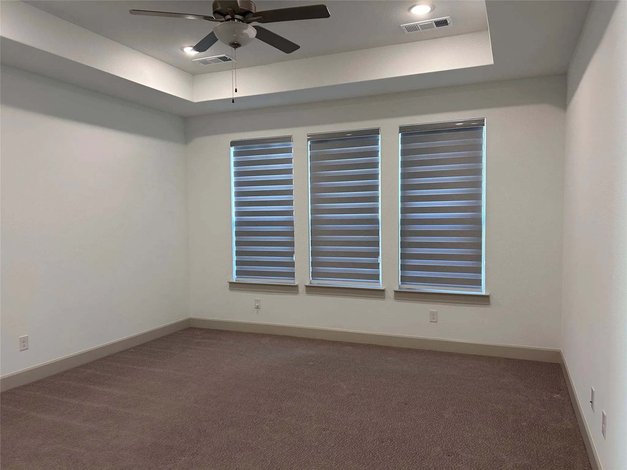 Spacious interior featuring a tray ceiling, recessed lighting, ceiling fan, three windows with blinds, and carpeting
