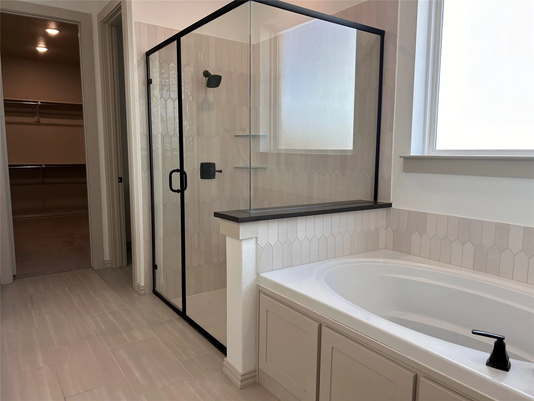 Freestanding soaking tub with tiled surround, walk-in shower with black-framed glass enclosure, and modern matte black fixtures