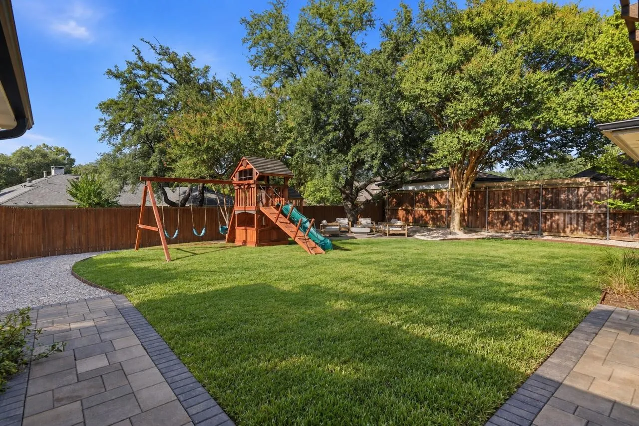 Expansive backyard featuring a manicured lawn, mature trees, and a privacy fence