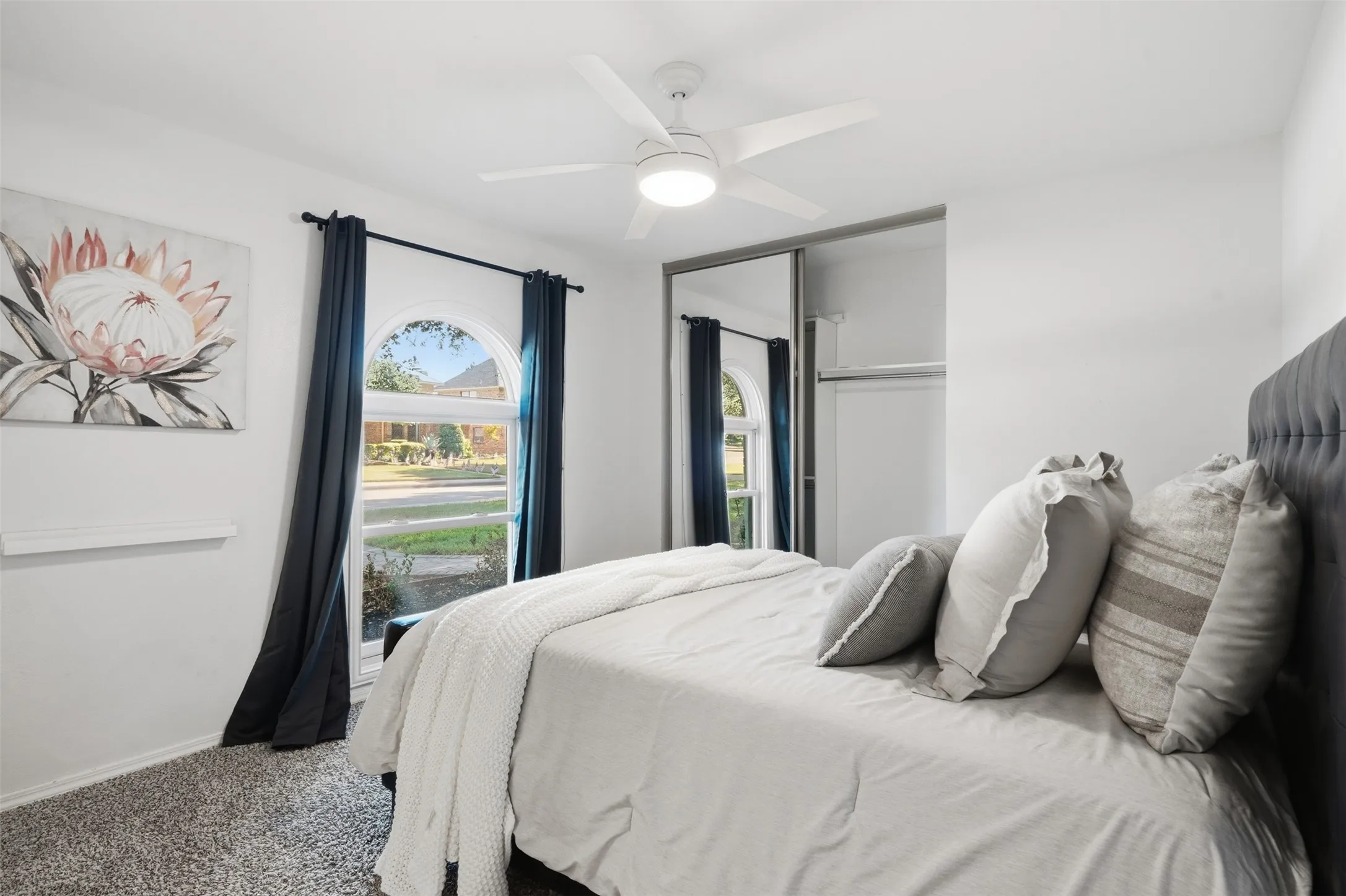 Bedroom with arched window, dark navy drapes, tufted bed headboard, and mirrored sliding closet doors