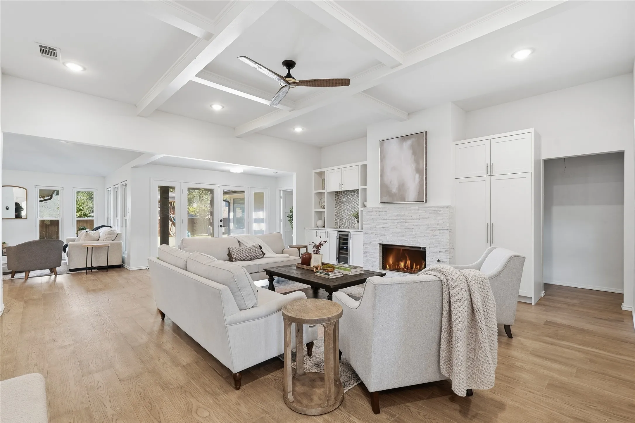 Wide angle view of modern open-concept living room with white sofas, coffered ceilings, and hardwood floors