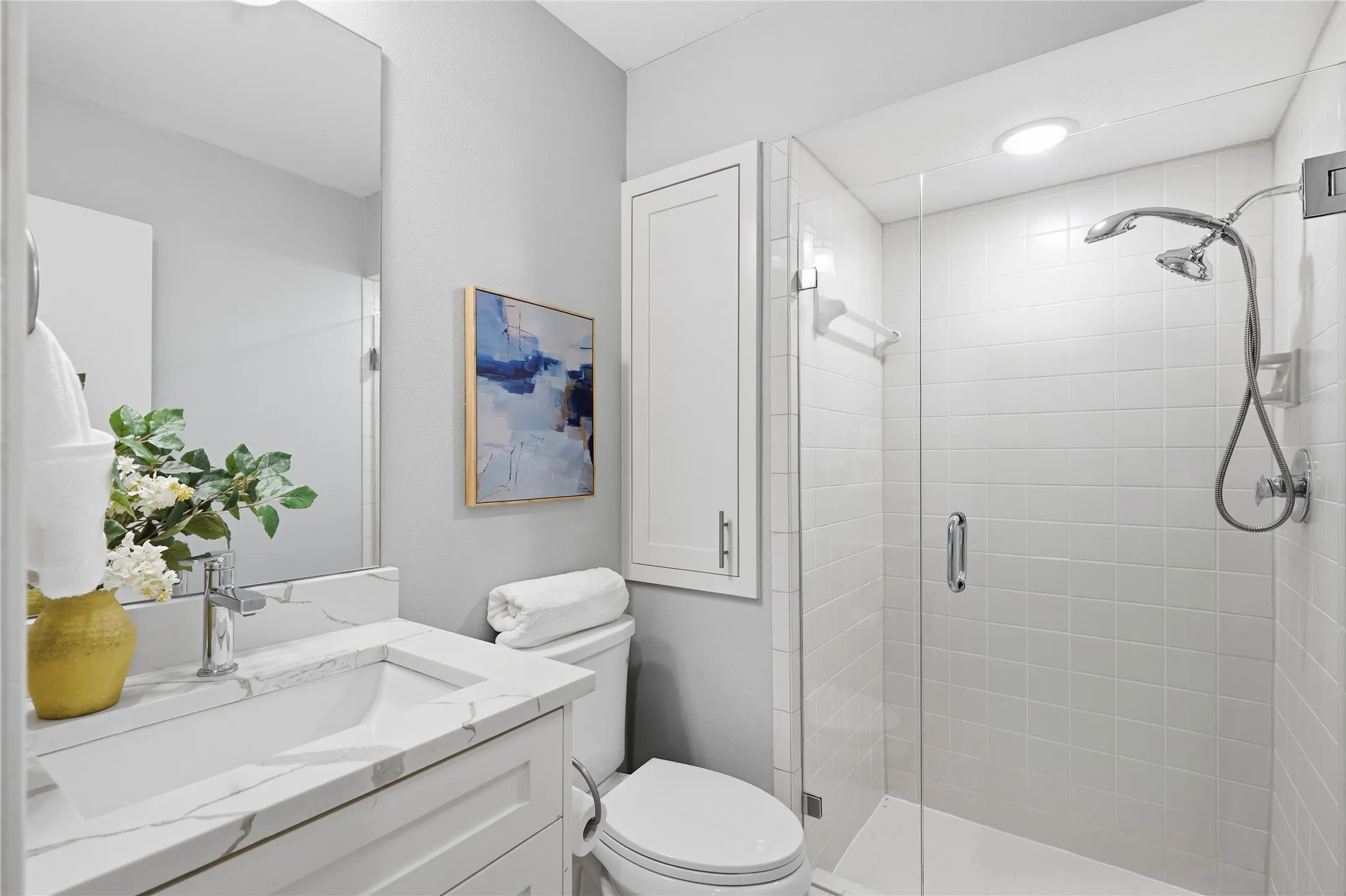 Modern guest bathroom with glass enclosure walk-in shower, white quartz vanity countertop, and frameless mirror