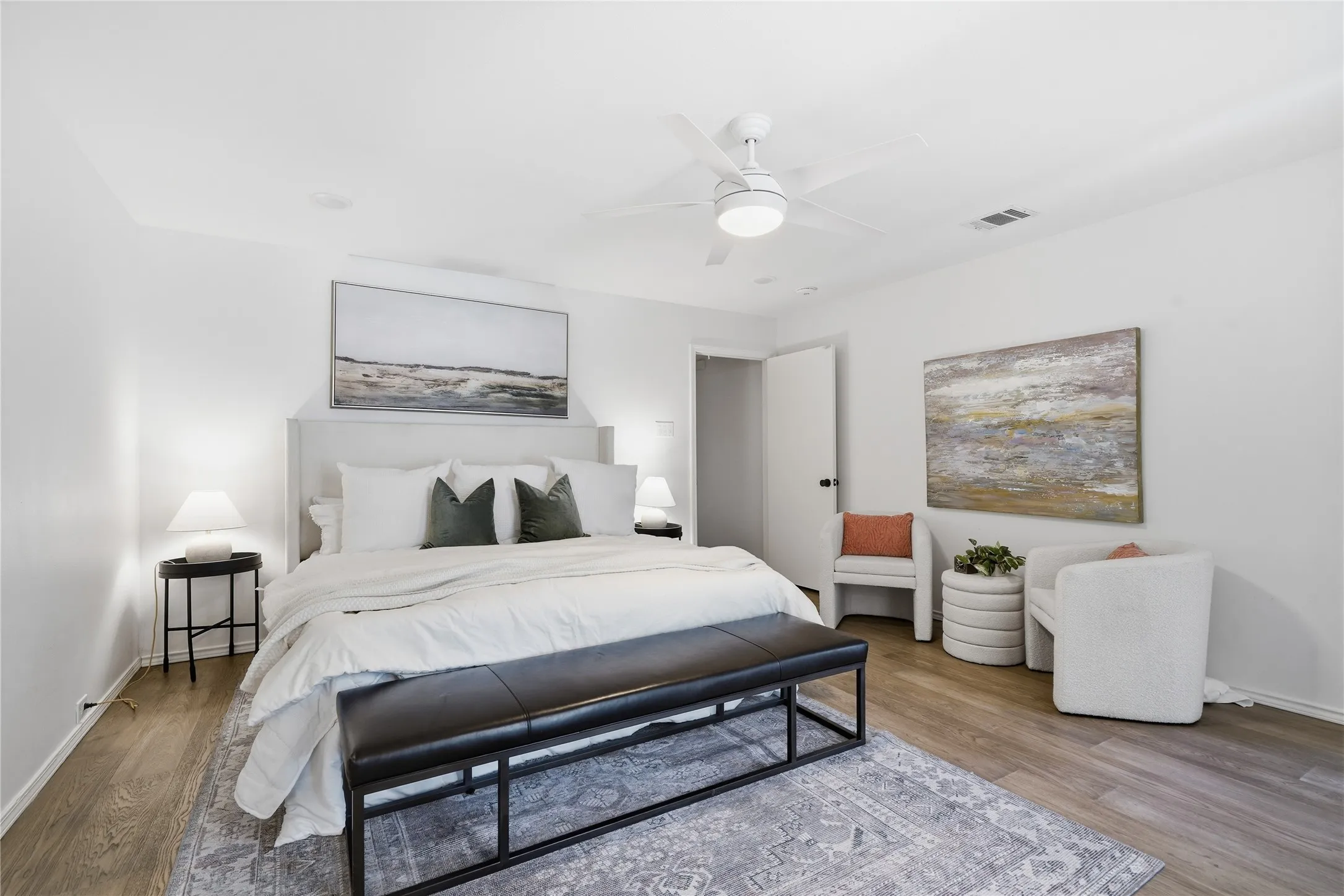 Primary bedroom suite featuring a king bed with white bedding, upholstered headboard, and black end bench
