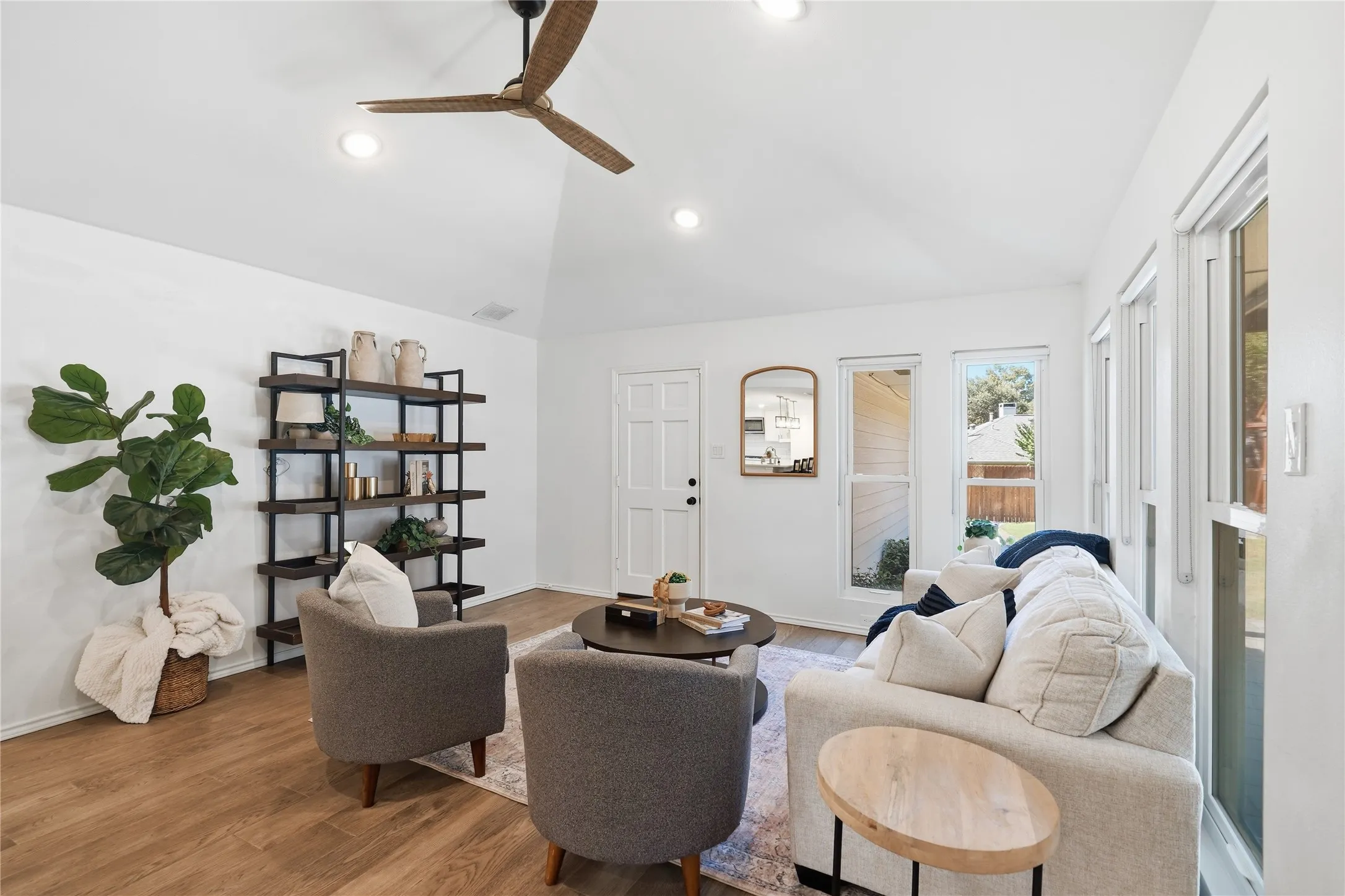 Sunroom sitting area with vaulted ceiling, grey armchairs, cream sofa, open bookshelf, and fiddle leaf fig plant