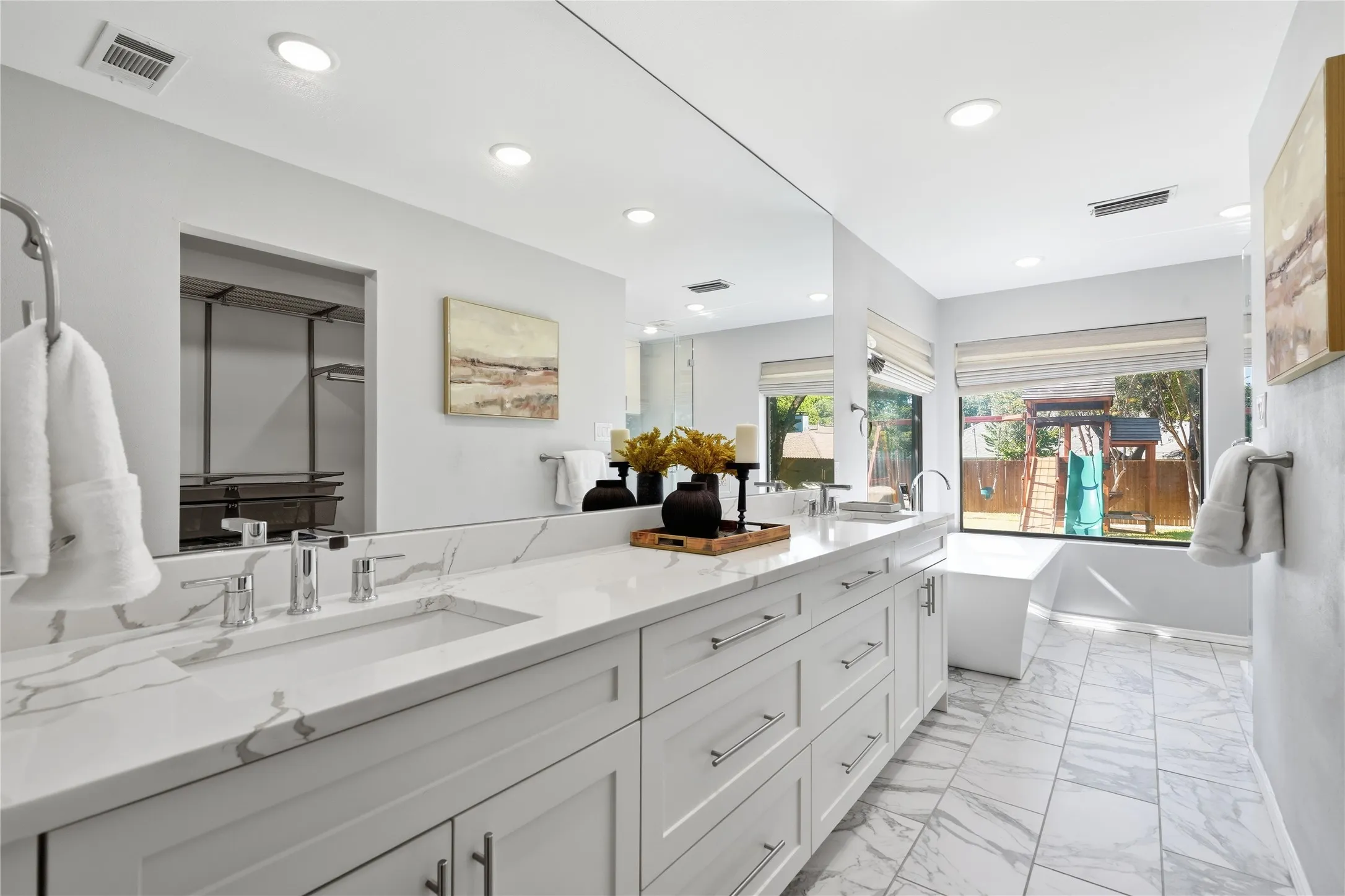Primary ensuite bathroom with white double sink vanity, full mirror, marble floor tile, and freestanding soaking tub