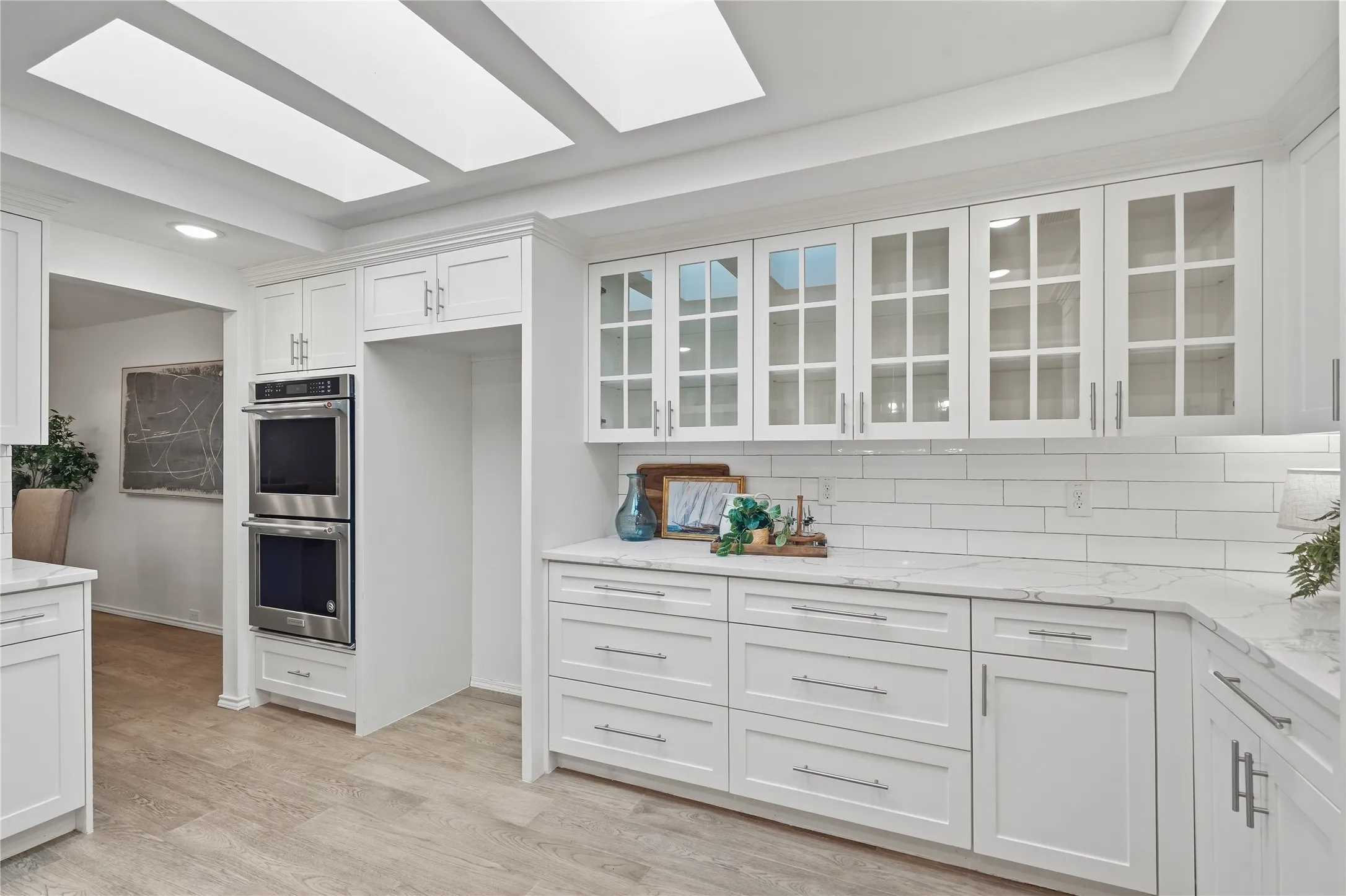 White kitchen cabinet wall with built-in stainless steel double wall ovens and glass front display cabinets