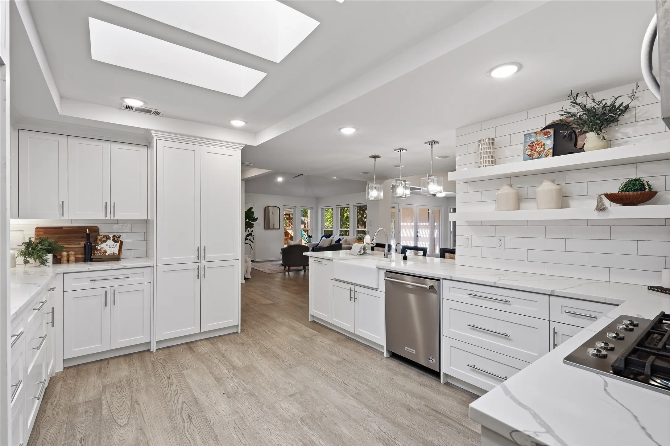 Modern white kitchen peninsula with quartz countertops, pendant lights, skylights, and open dining access