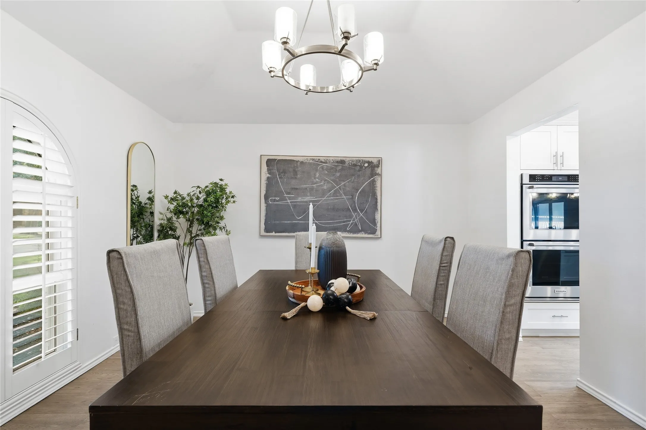 Formal dining room featuring a dark wood dining table, grey upholstered chairs, modern chandelier, and arched shuttered doors