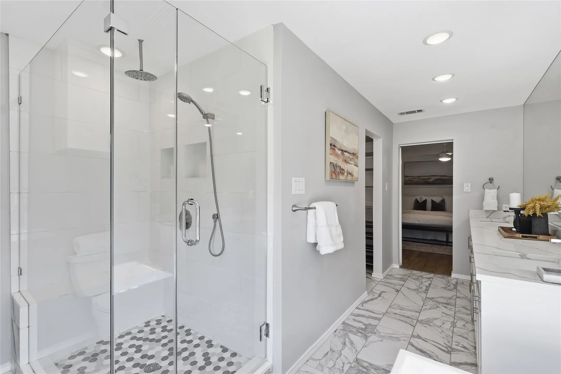 Primary bathroom walk-in shower with frameless glass door, rain shower head, and grey marble hexagon floor tile