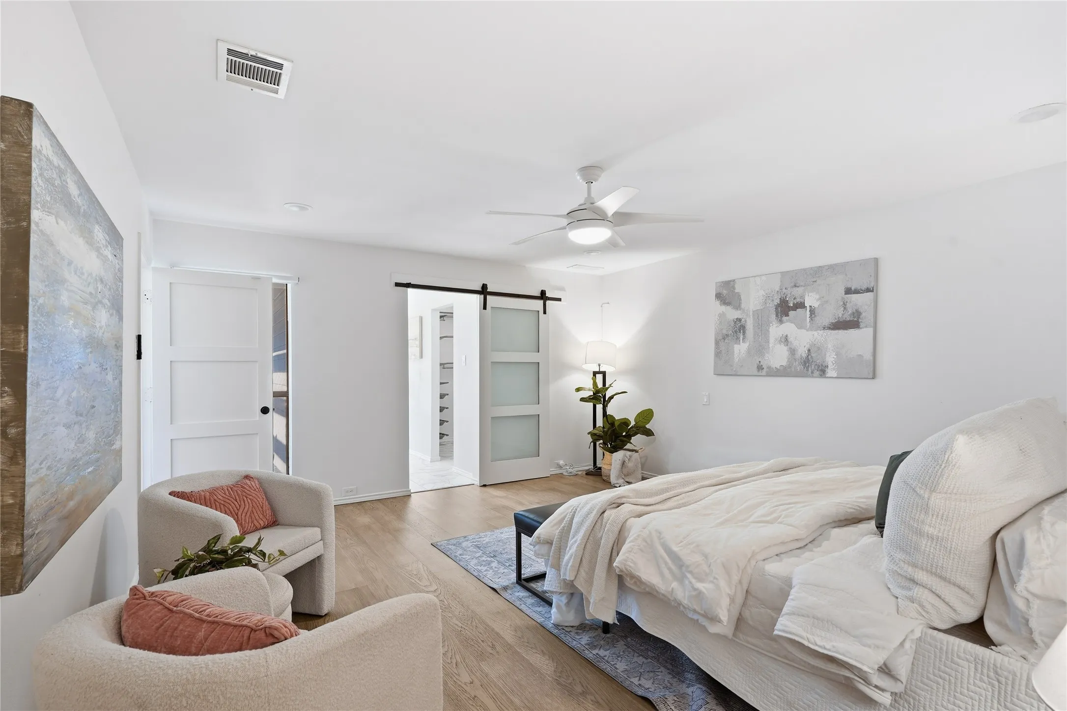 Primary bedroom suite sitting area with cream bouclé armchairs and a modern white sliding barn door