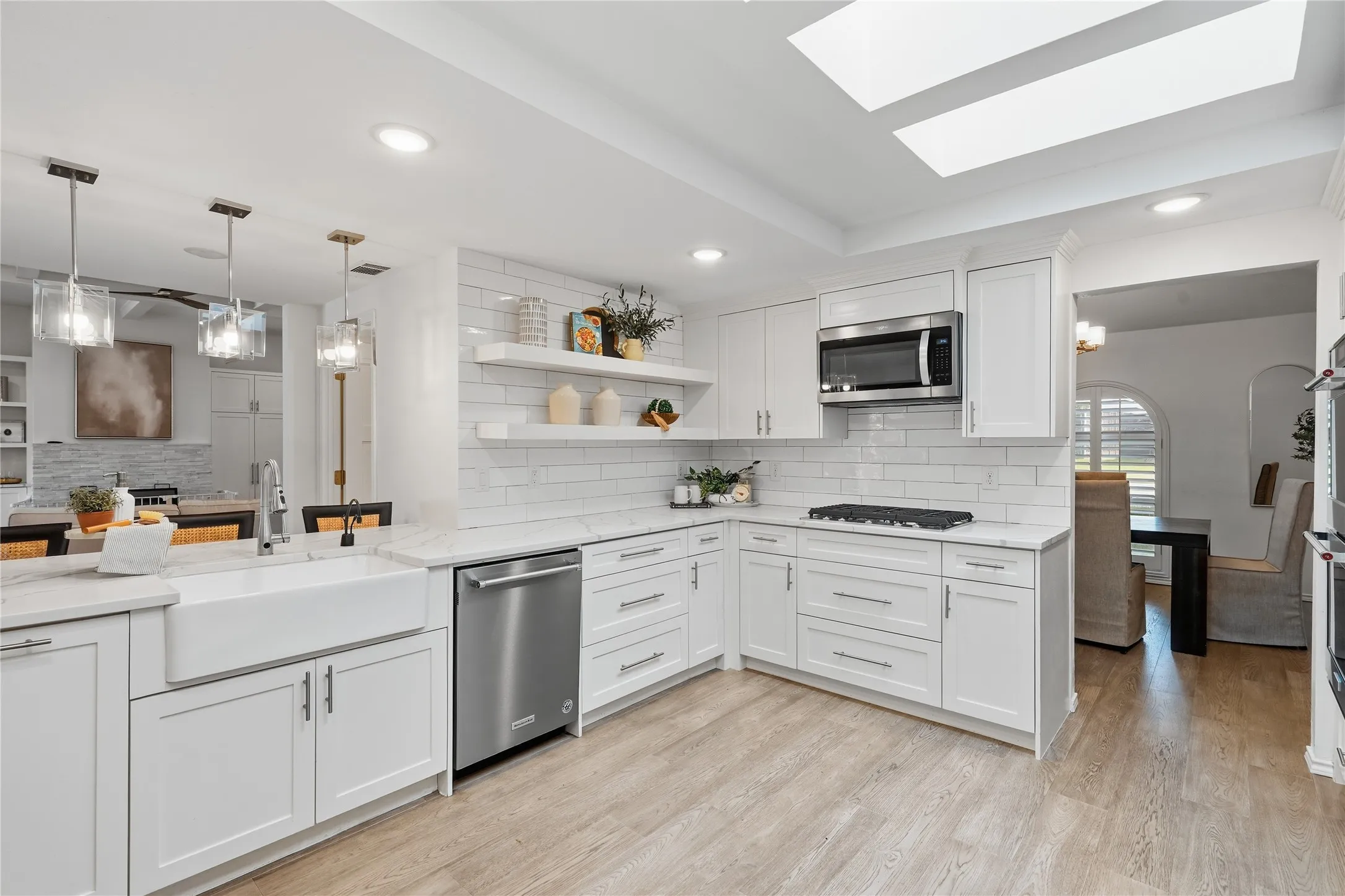 Bright white kitchen remodel with apron-front farmhouse sink, subway tile backsplash, floating shelves, and skylights

