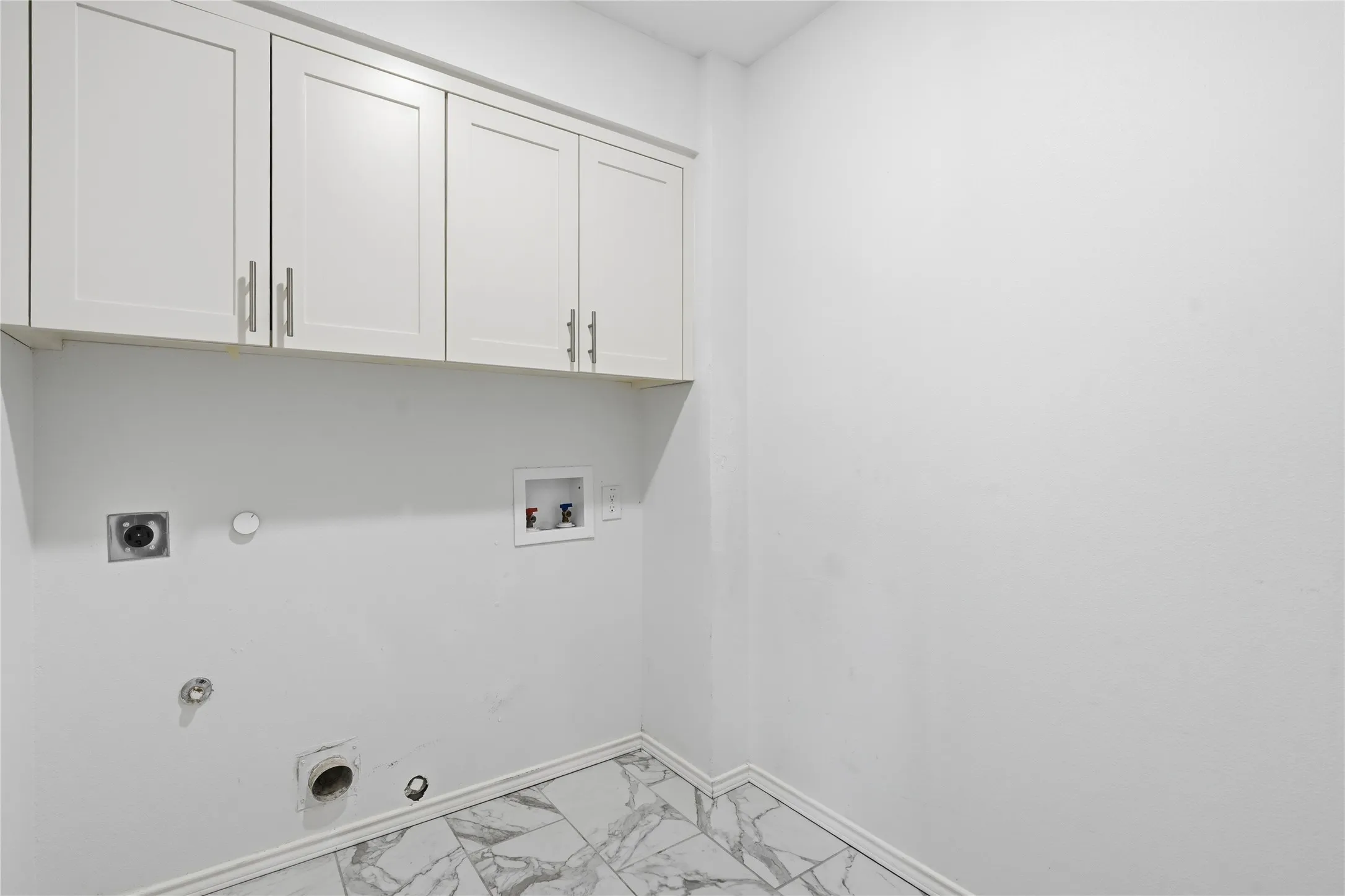 Modern white utility laundry room with upper shaker cabinets, marble floor tiles, and washer dryer hookups