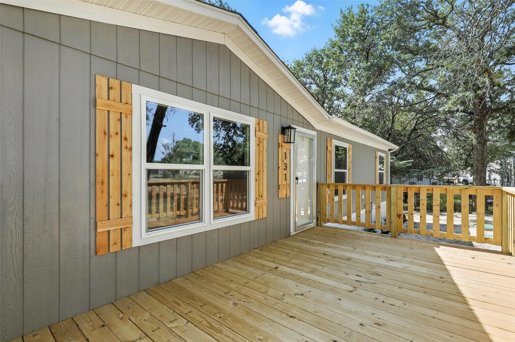 Front exterior with vertical siding, wood-finish shutters, and a wood-finish deck with railings