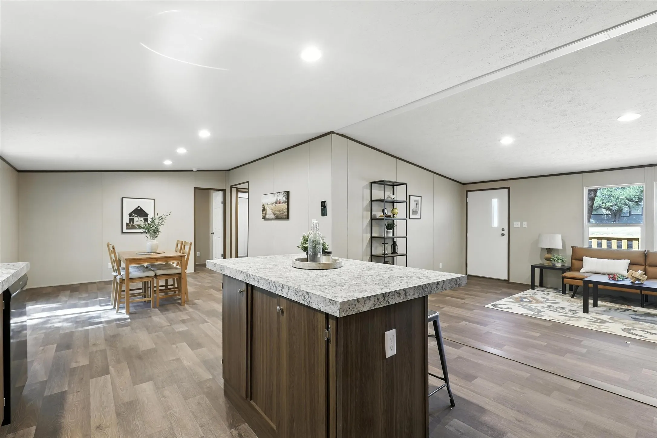 Open-concept living space with recessed lighting, wood-finish flooring, a kitchen island with a stone-finish countertop, and built-in shelving