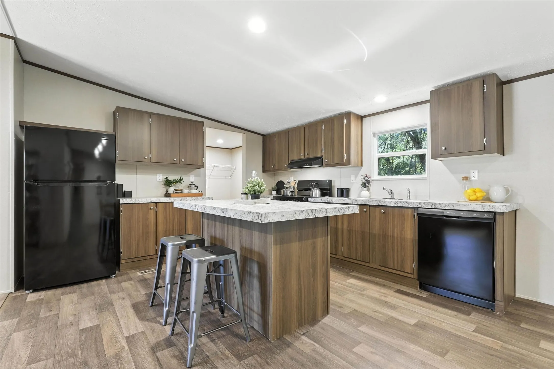 Kitchen featuring wood-finish flooring, wood-toned cabinetry, a spacious island with a countertop, black appliances, and recessed lighting