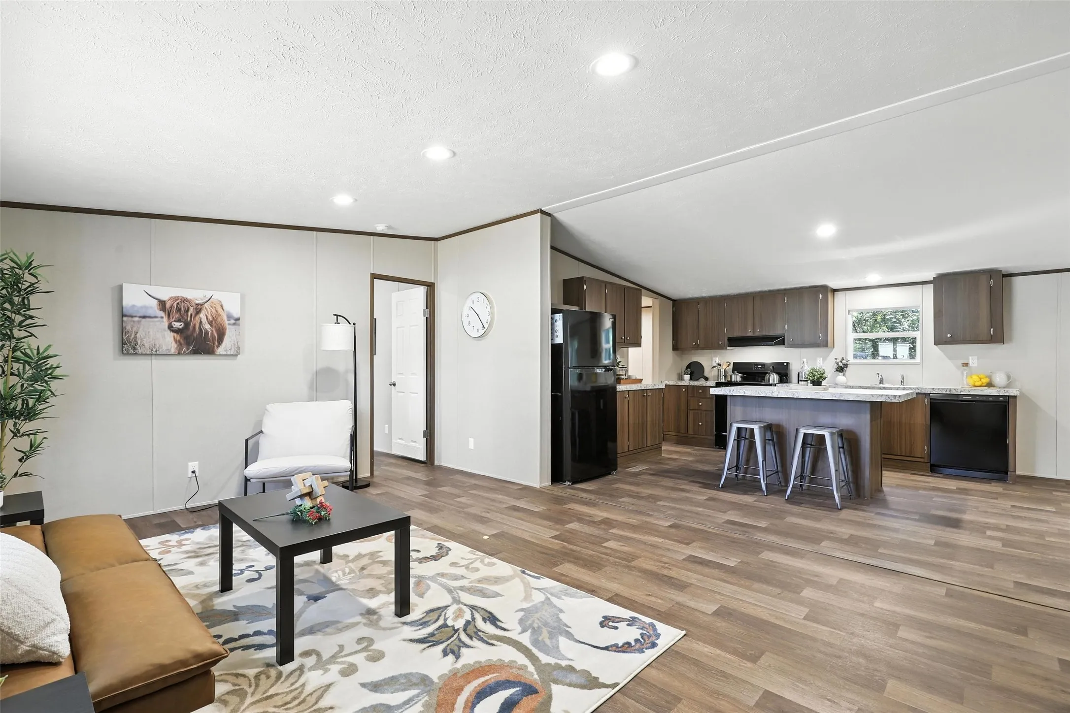 Open-concept living area with wood-finish flooring, recessed lighting, and a kitchen island with seating