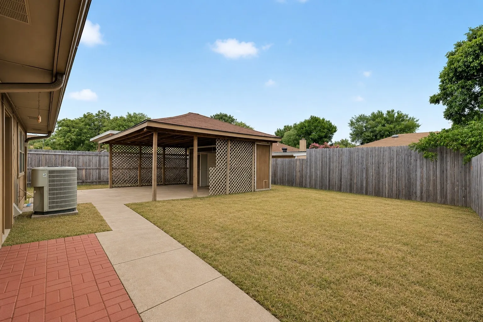 Expansive backyard featuring a covered patio, concrete pathway, red brick patio, and privacy fencing