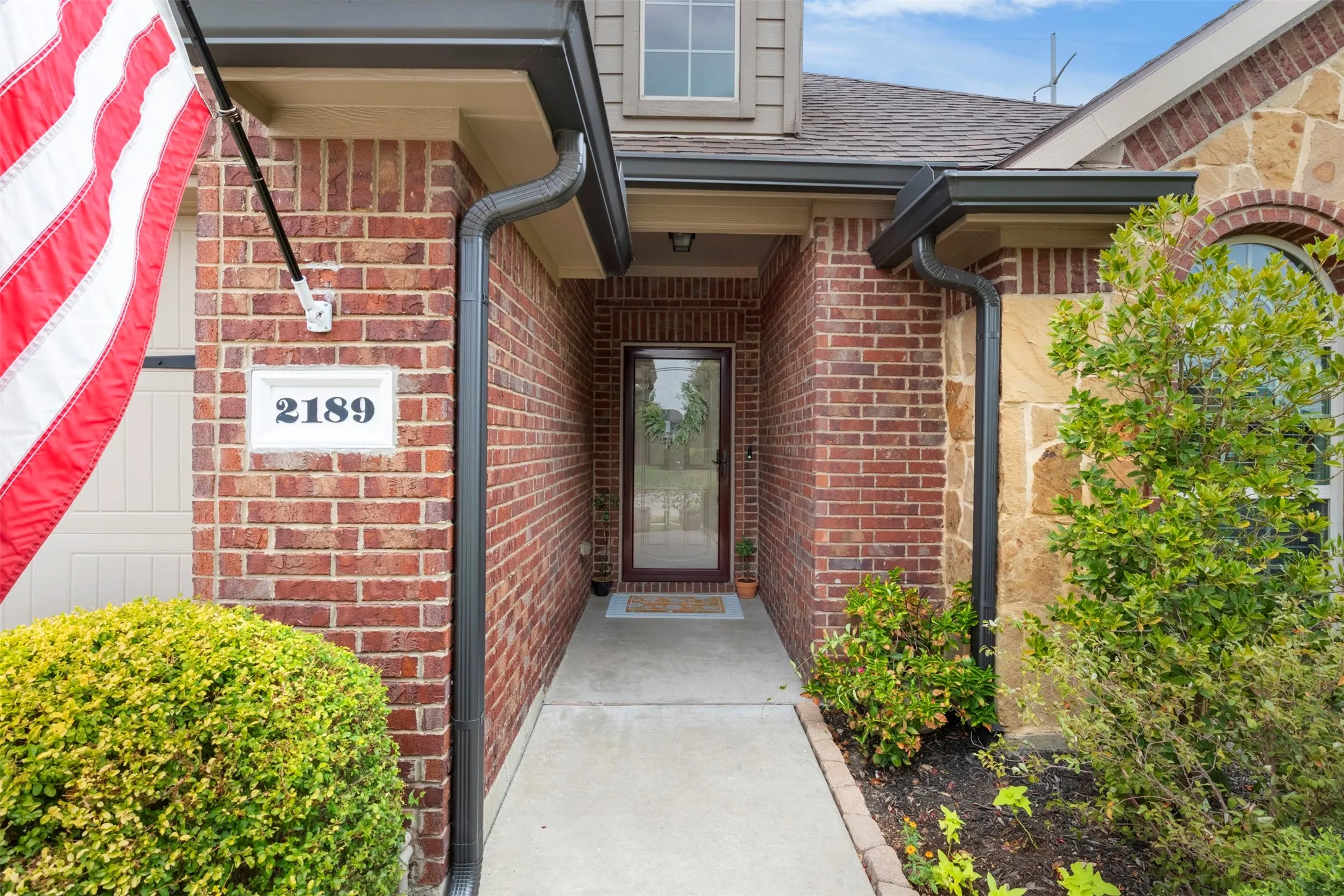 A closer look at the covered front entry, framed by brick and stone details and established landscaping—a welcoming transition into the home's updated interior.