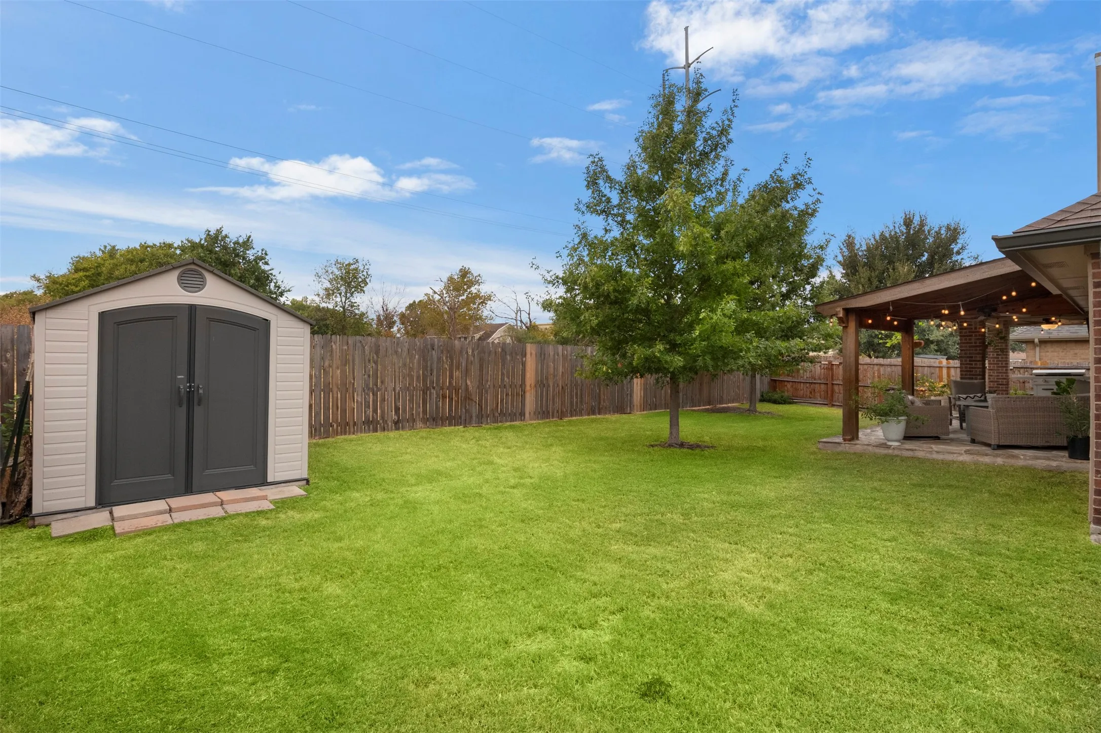 Spacious fenced yard with mature shade trees and a separate storage shed.