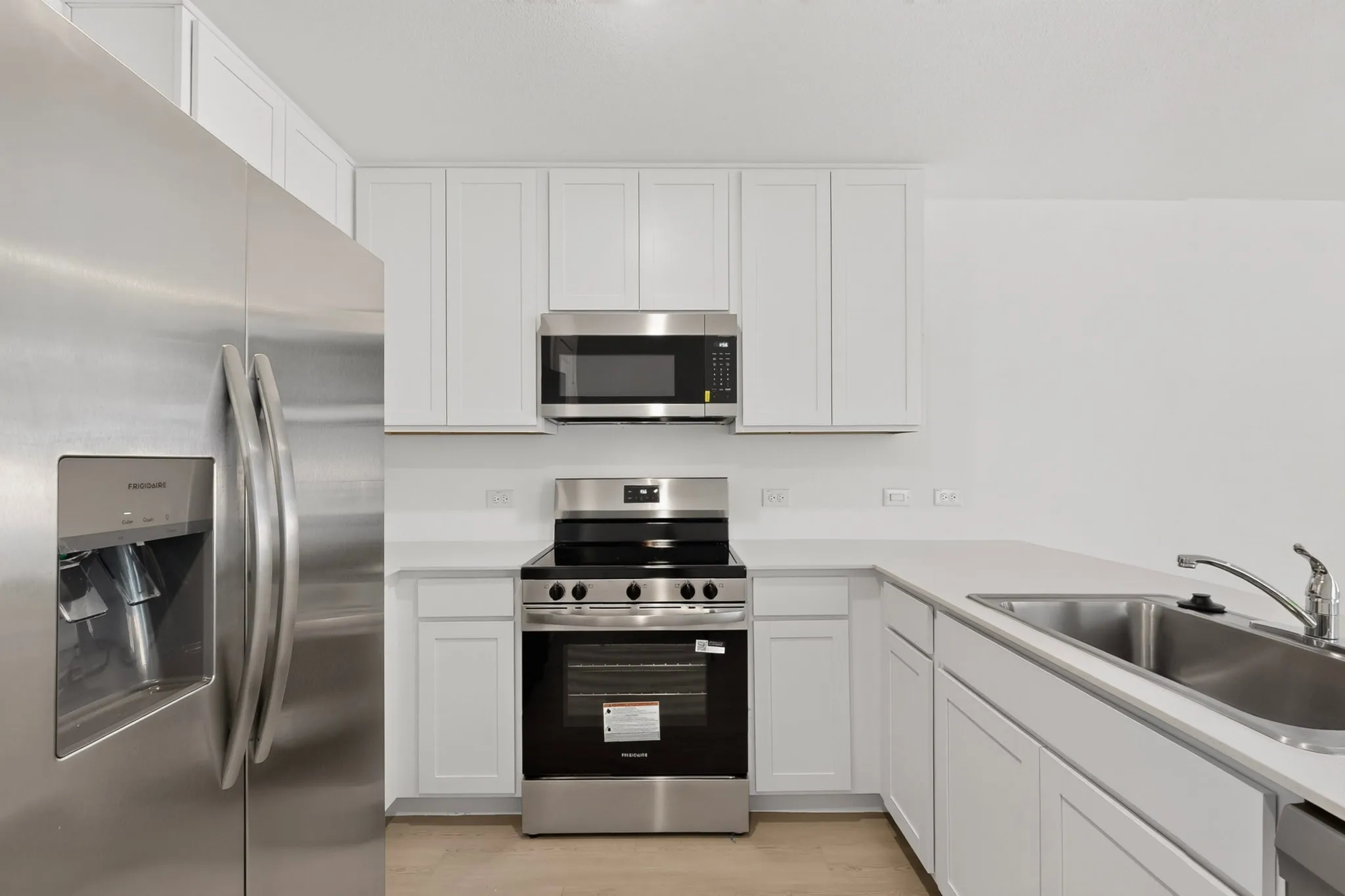 Stainless steel appliances, white cabinetry, integrated sink, and light-toned countertops