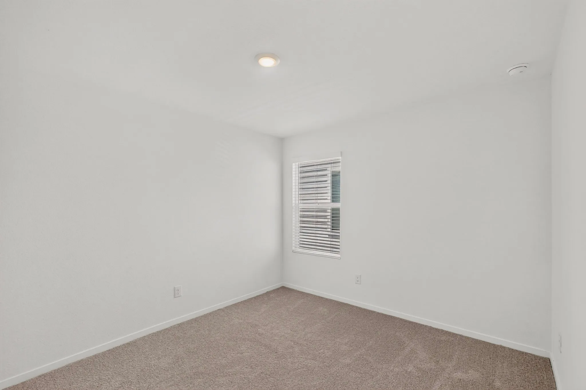 Recessed ceiling lighting, a window with horizontal blinds, and neutral wall paint