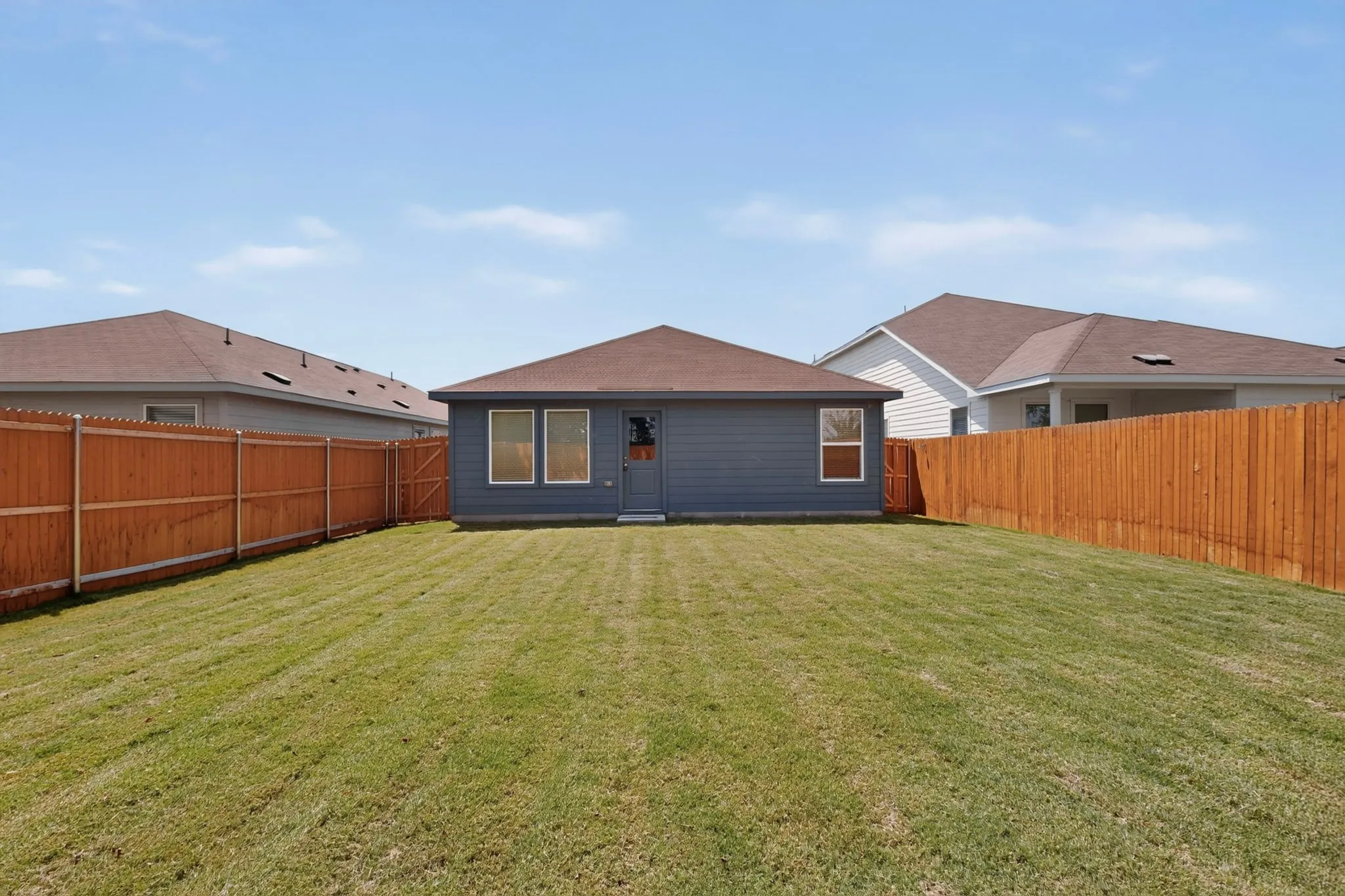 Expansive fenced backyard featuring a wood privacy fence, a well-maintained lawn, and a rear exterior with multiple windows