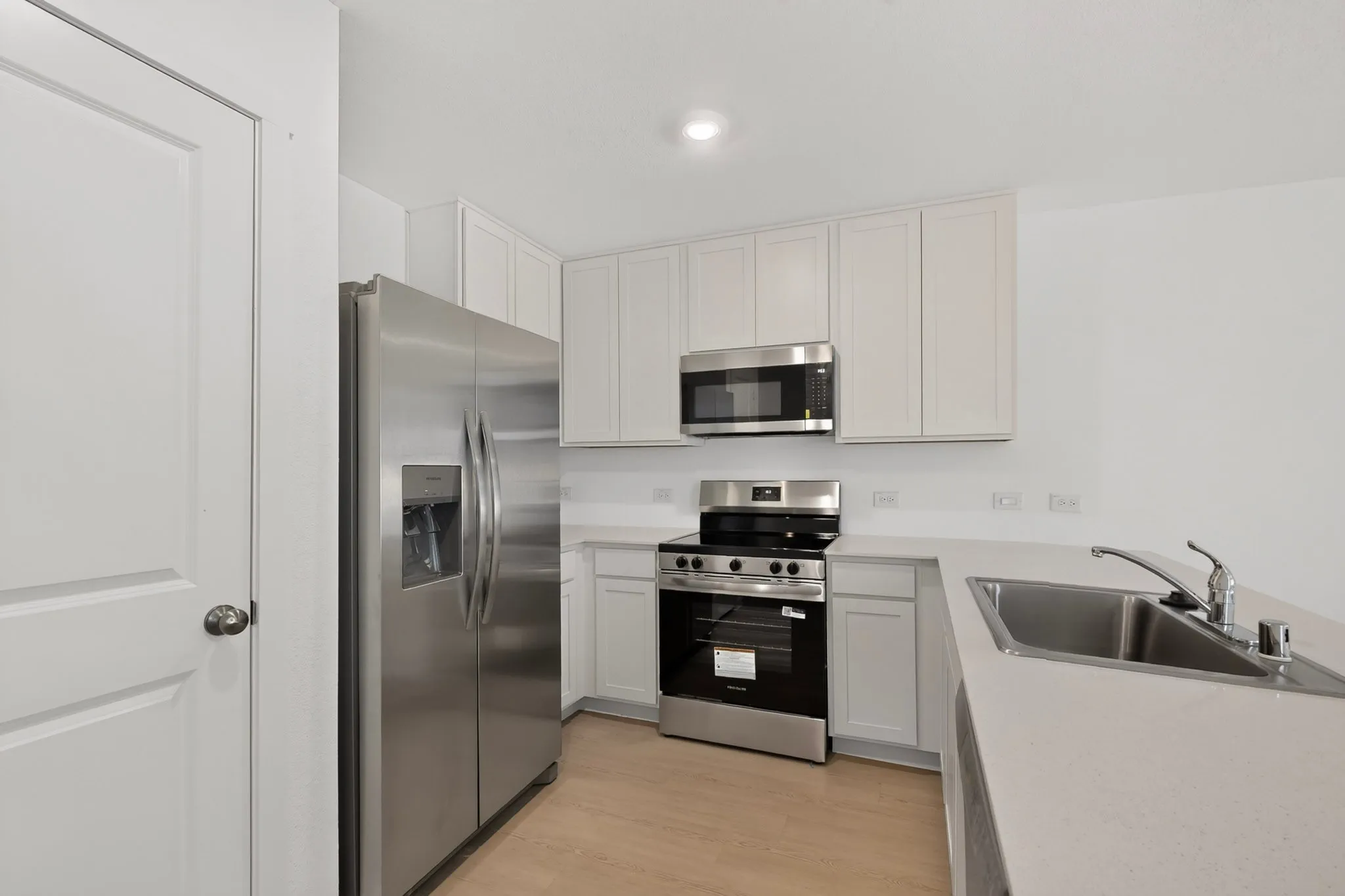 Contemporary kitchen featuring stainless steel appliances, light wood-finish flooring, white cabinetry, and light-toned countertops