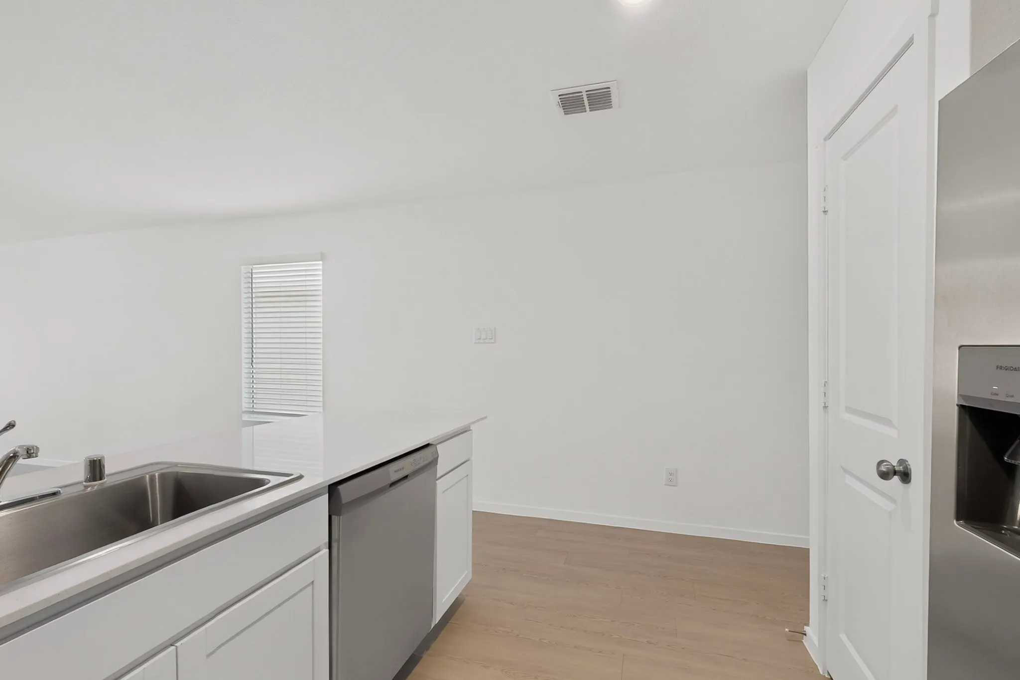 Kitchen island with a stainless steel sink, white cabinetry, integrated dishwasher, and light wood-finish flooring