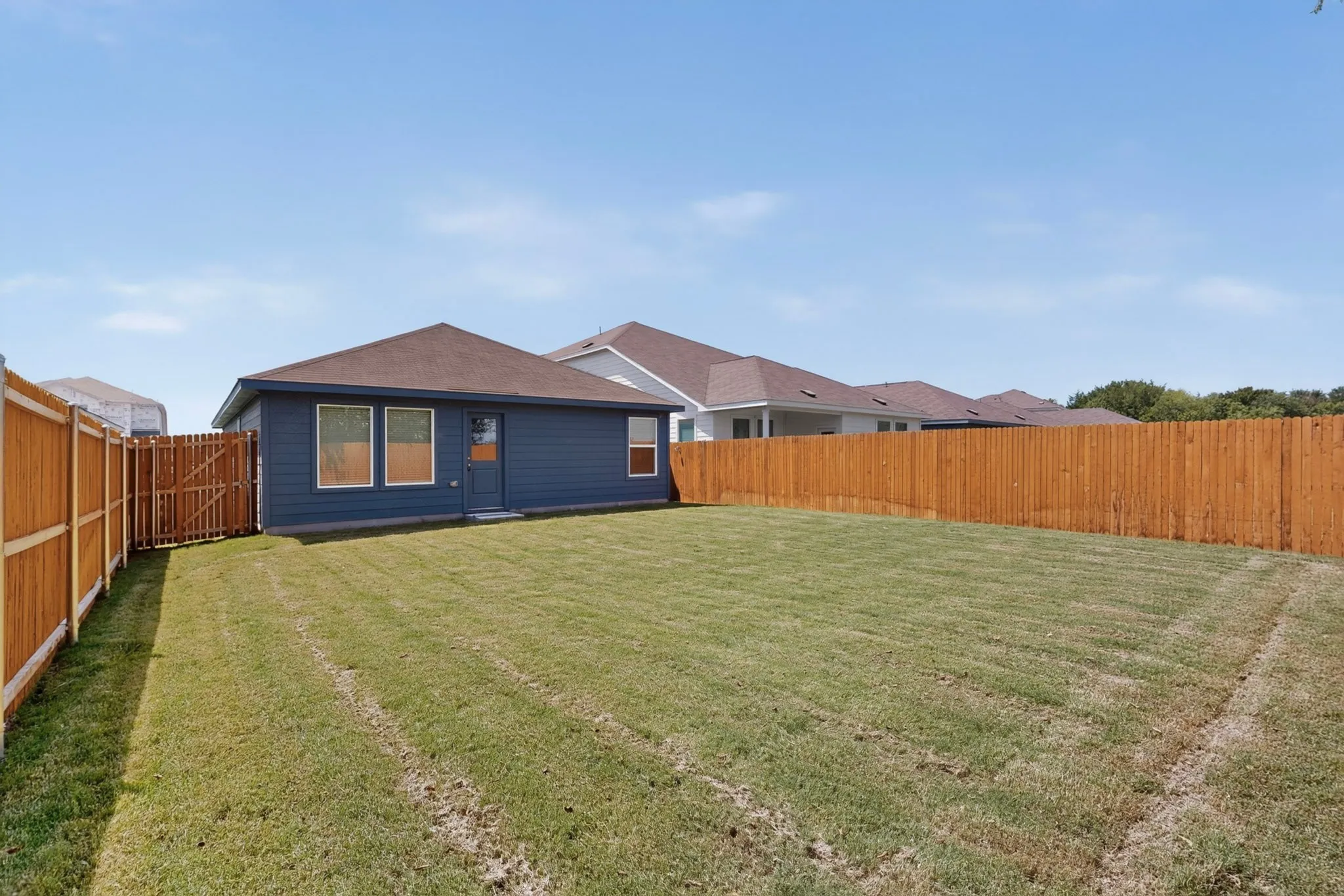 Expansive backyard featuring a manicured lawn, wood privacy fencing, and a rear exterior with a dark siding finish