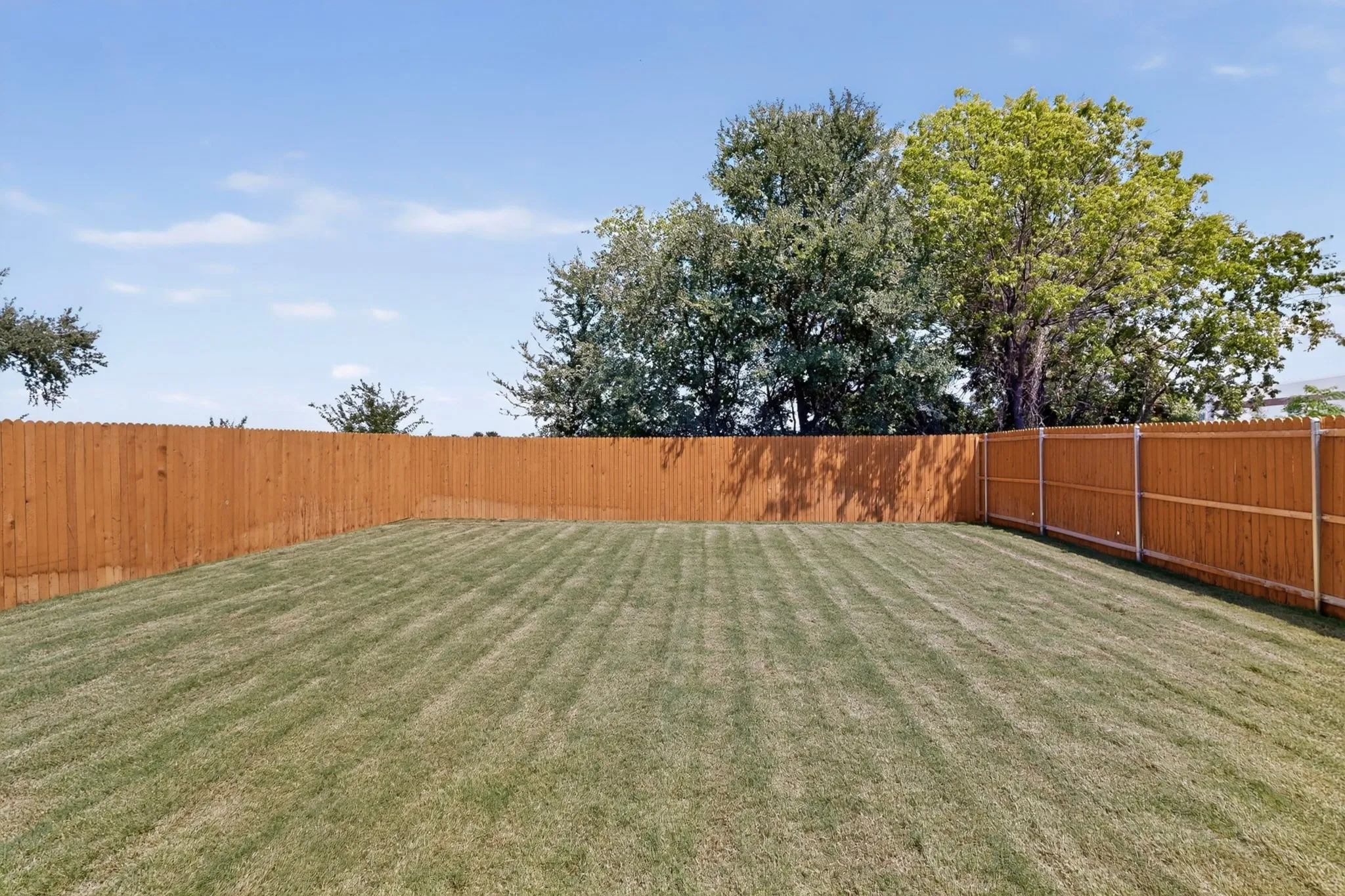 Expansive backyard featuring a manicured lawn, a full wood privacy fence, and mature trees