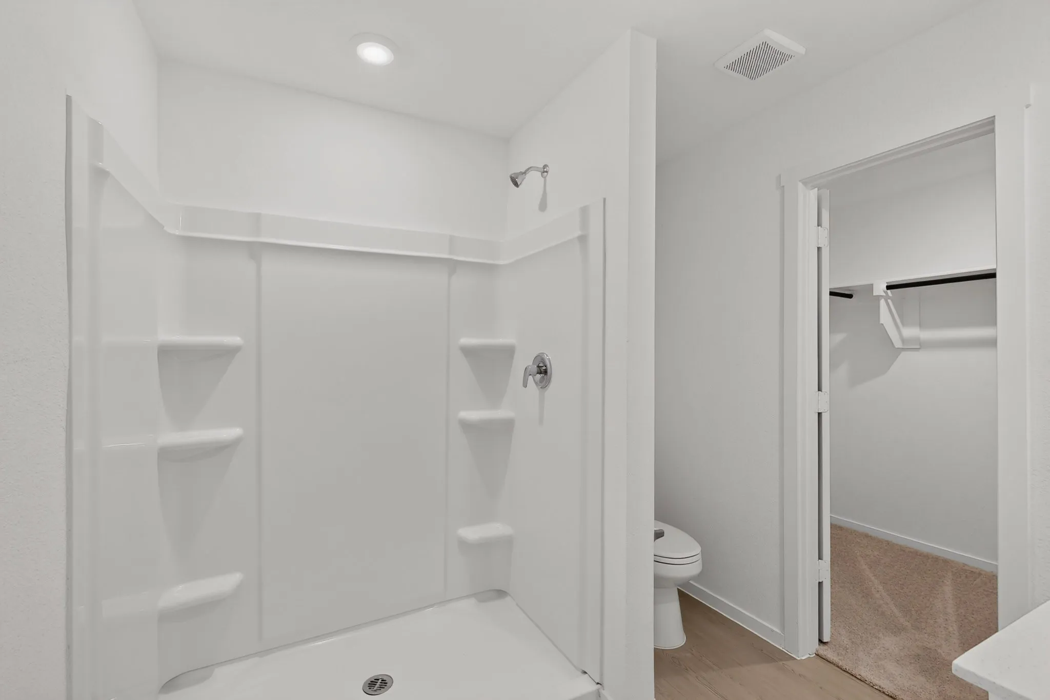 White shower enclosure with built-in shelving, chrome fixtures, and a recessed ceiling light