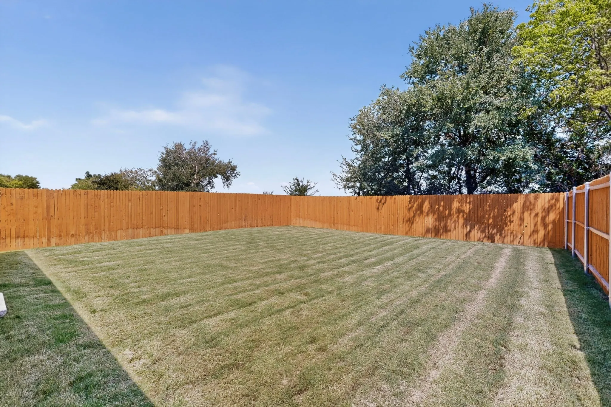 Expansive backyard featuring a manicured lawn, full wood fencing, and mature perimeter trees