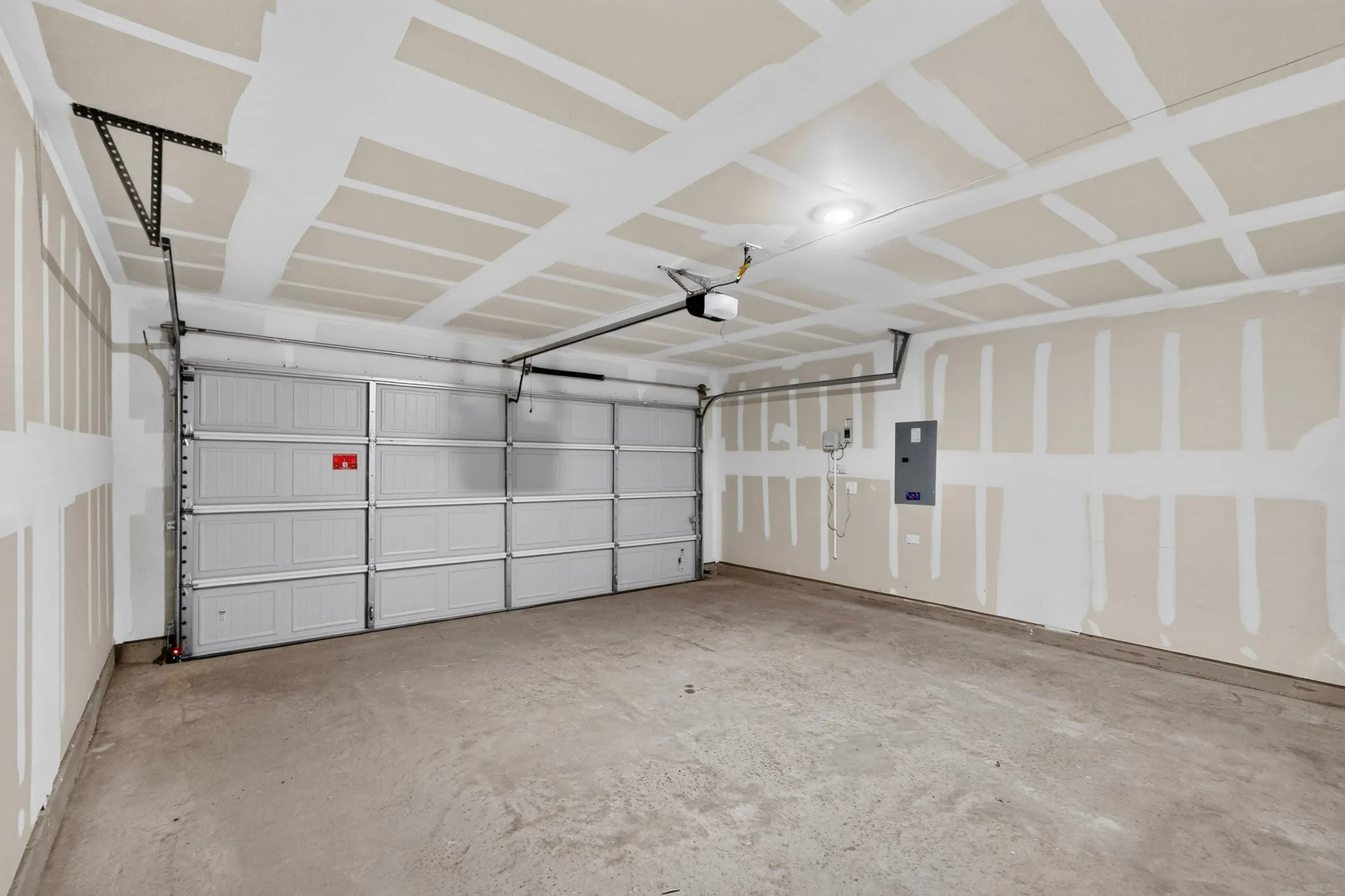 Spacious garage featuring a panel garage door, exposed ceiling joists, concrete flooring, and an electrical panel