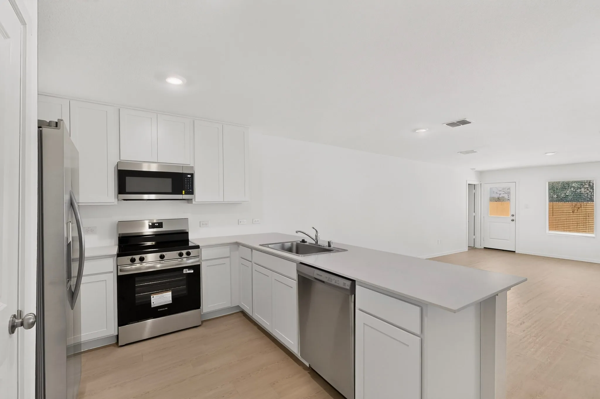 Kitchen featuring stainless steel appliances, white cabinetry, a kitchen island with a double basin sink, and wood-finish flooring