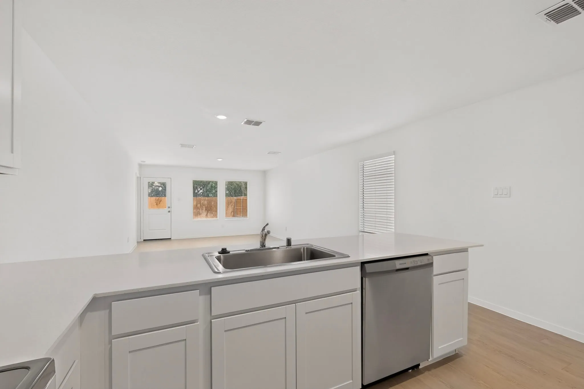 Central kitchen island with an undermount sink, stainless steel dishwasher, white shaker cabinetry, and light-toned countertops