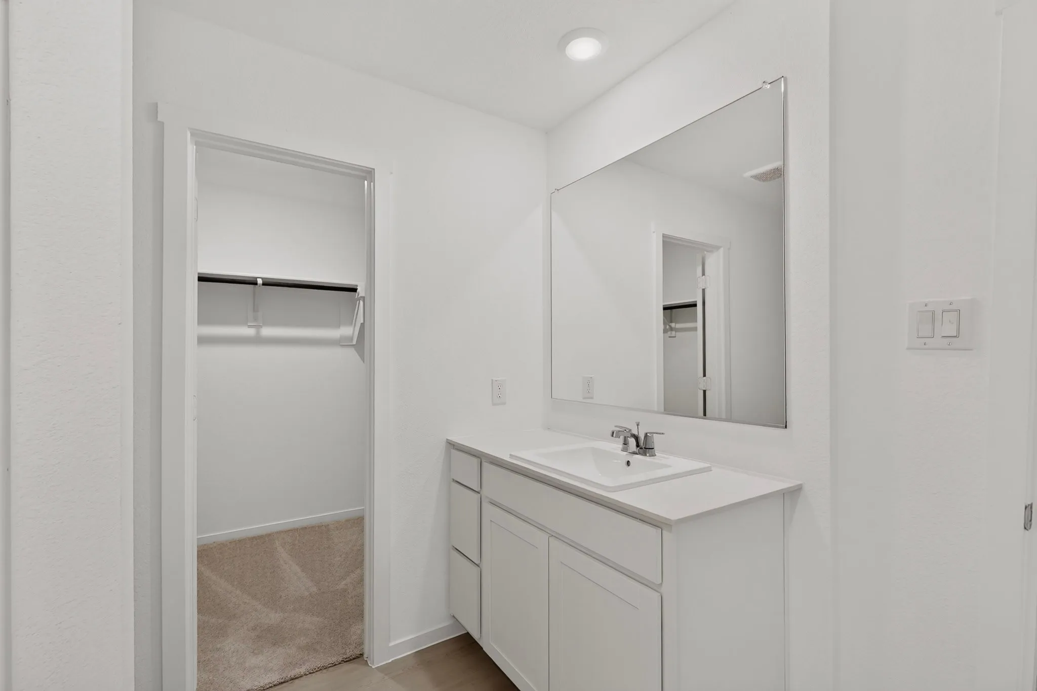 White vanity with an integrated rectangular sink, chrome faucet, and expansive wall-mounted mirror