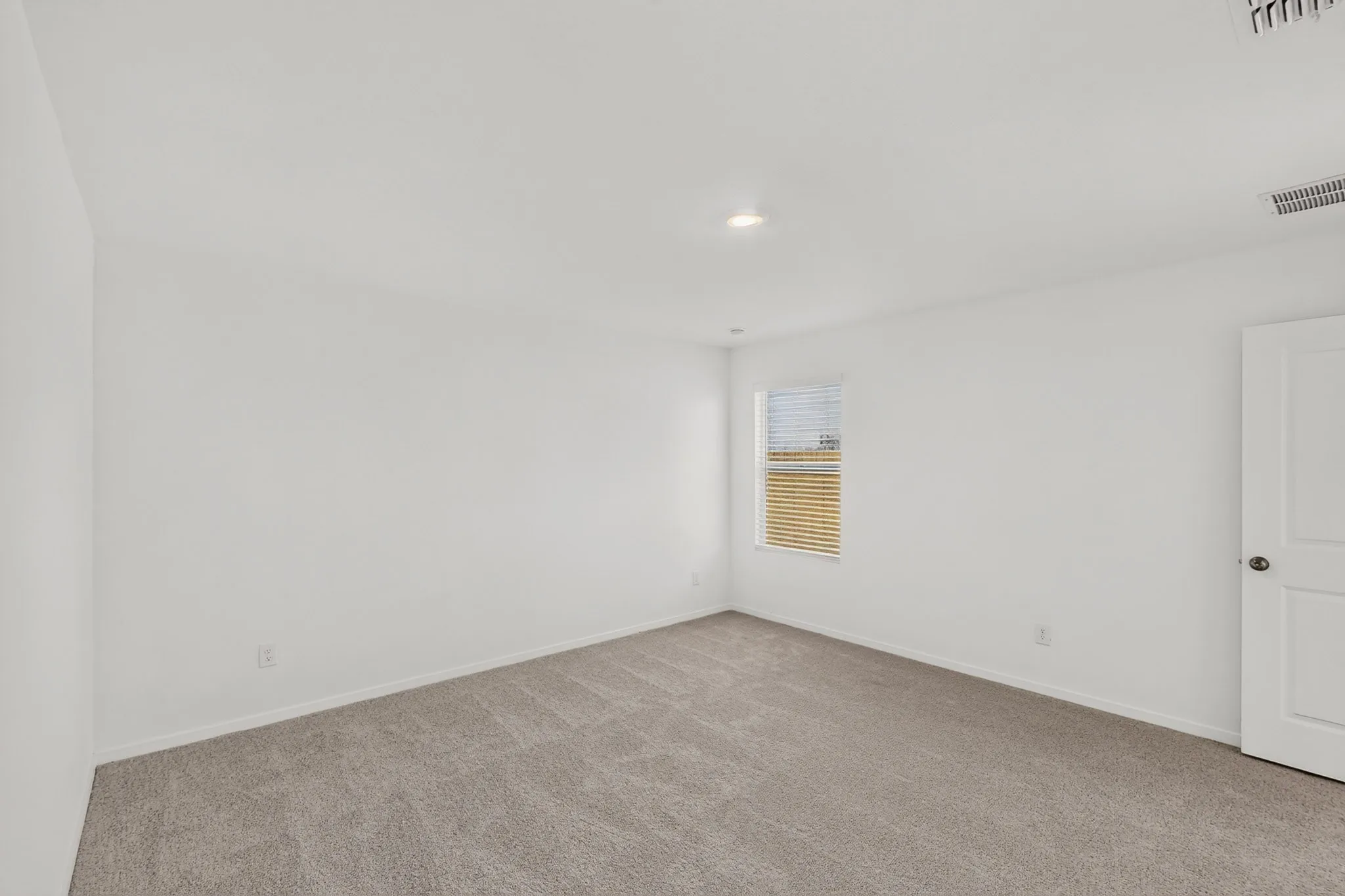 Recessed lighting, neutral wall paint, light gray carpet, window with blinds, and white interior door