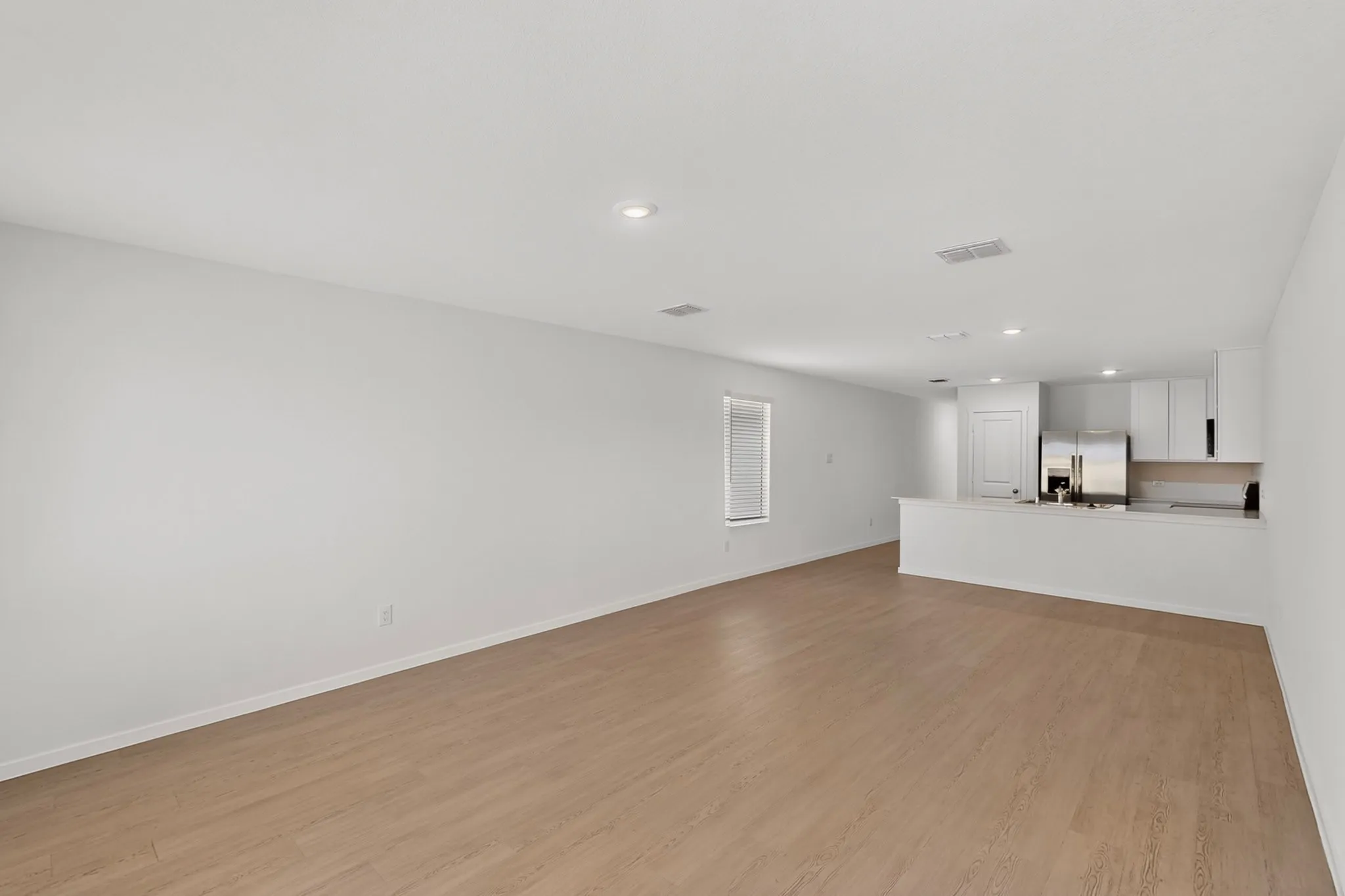 Open-concept living area featuring wood-finish flooring, recessed lighting, and a kitchen with white cabinetry and stainless steel appliances