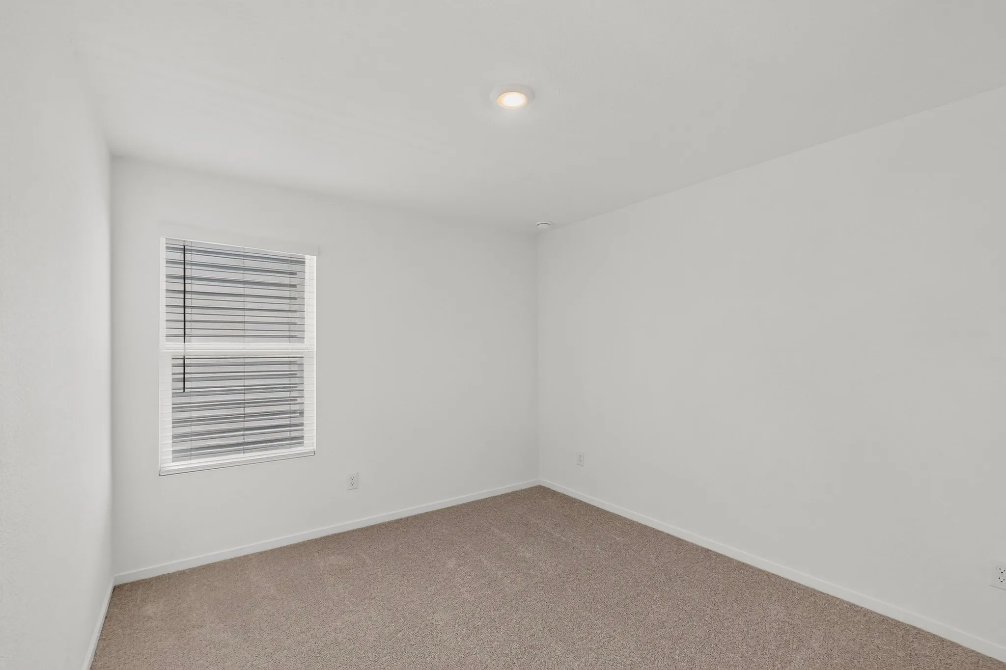 Recessed ceiling lighting, neutral carpet flooring, and window with horizontal blinds
