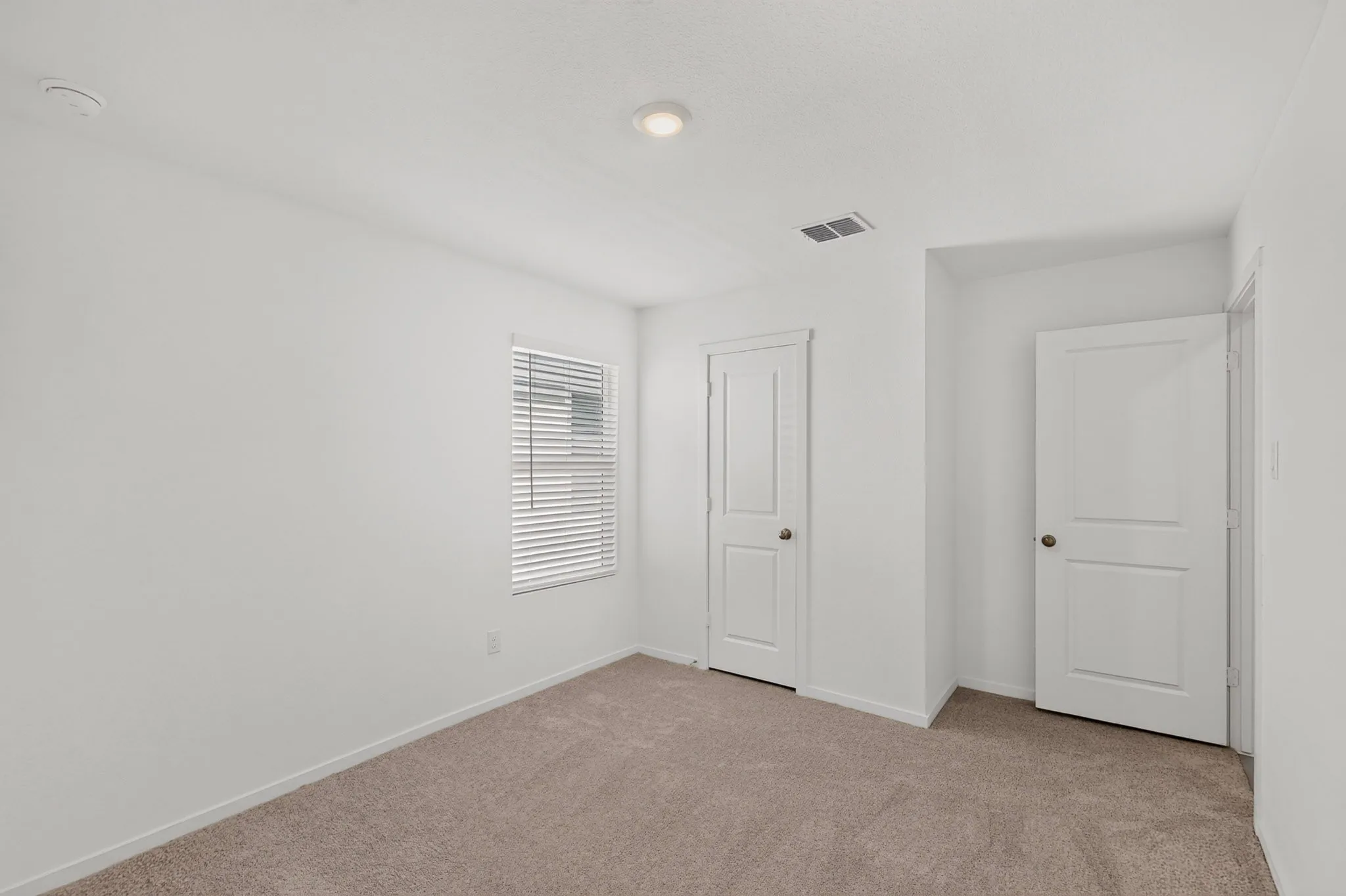 Neutral tone wall finishes, recessed ceiling lighting, light-colored carpeting, white paneled doors, and a window with blinds