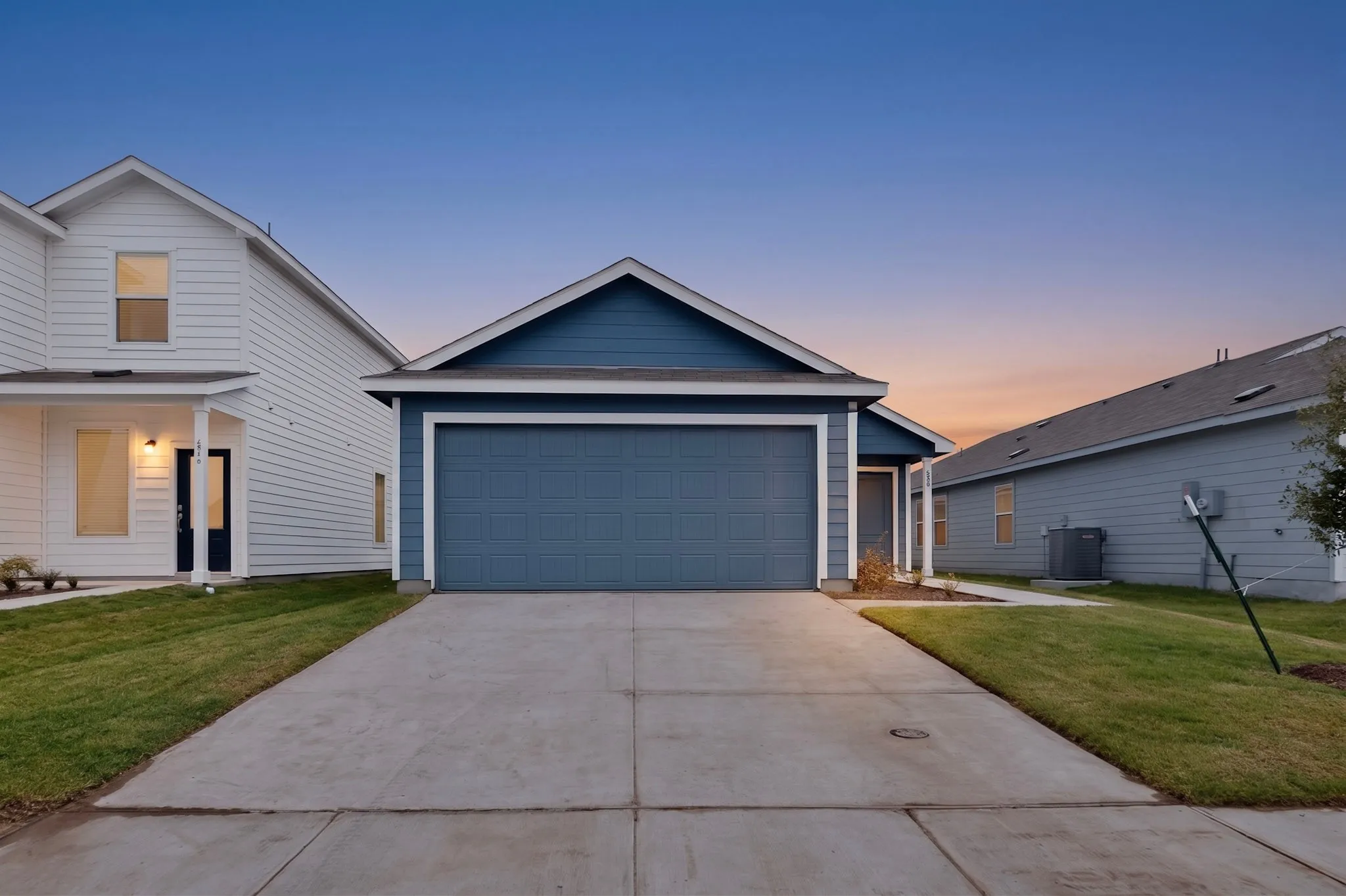 Siding exterior with a gable roofline, attached garage, concrete driveway, and manicured lawn