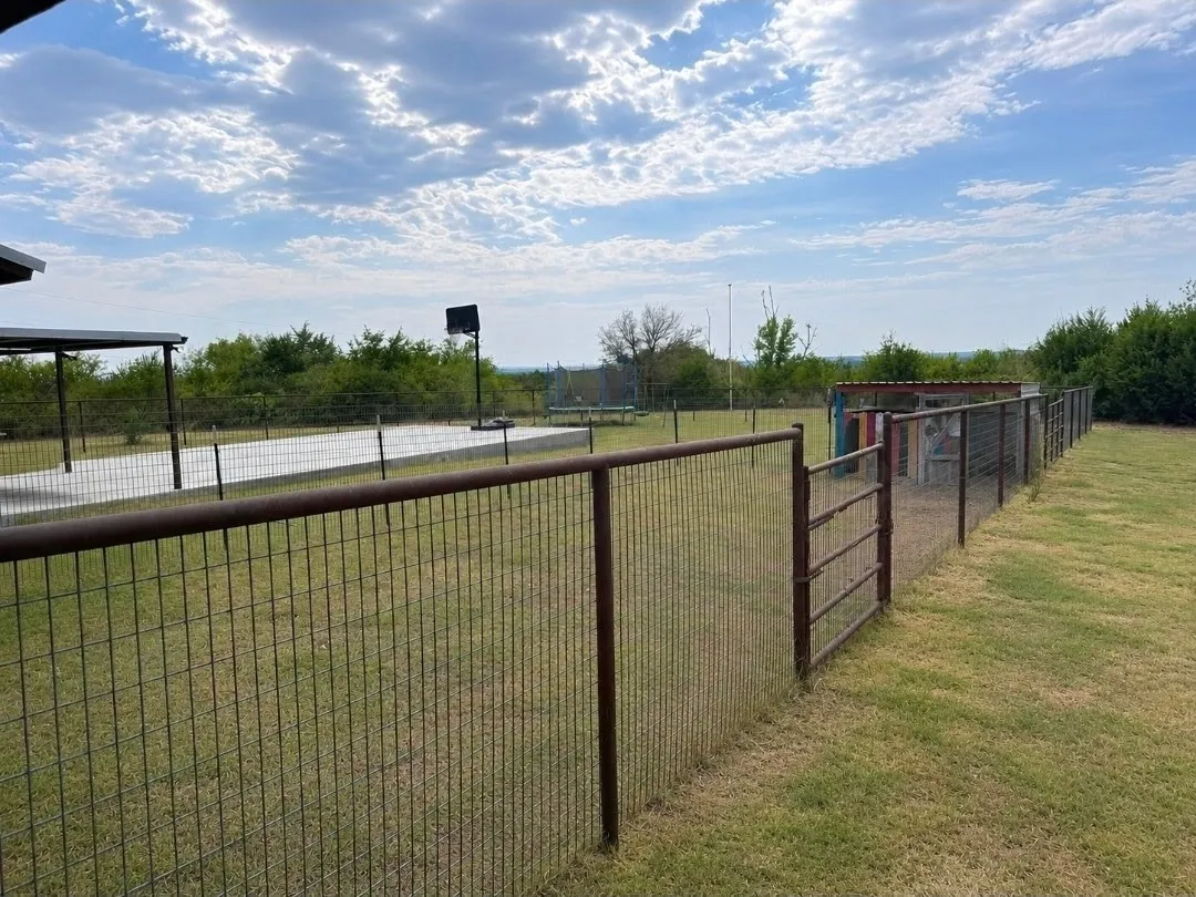 Expansive outdoor space featuring a large concrete court, partial covered patio, metal fencing, and a separate fenced enclosure