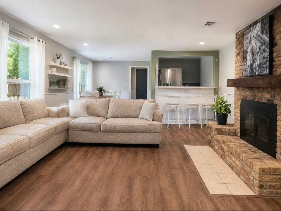 Warm wood-finish flooring, brick fireplace with a wood mantle, recessed lighting, and a breakfast bar with white paneling